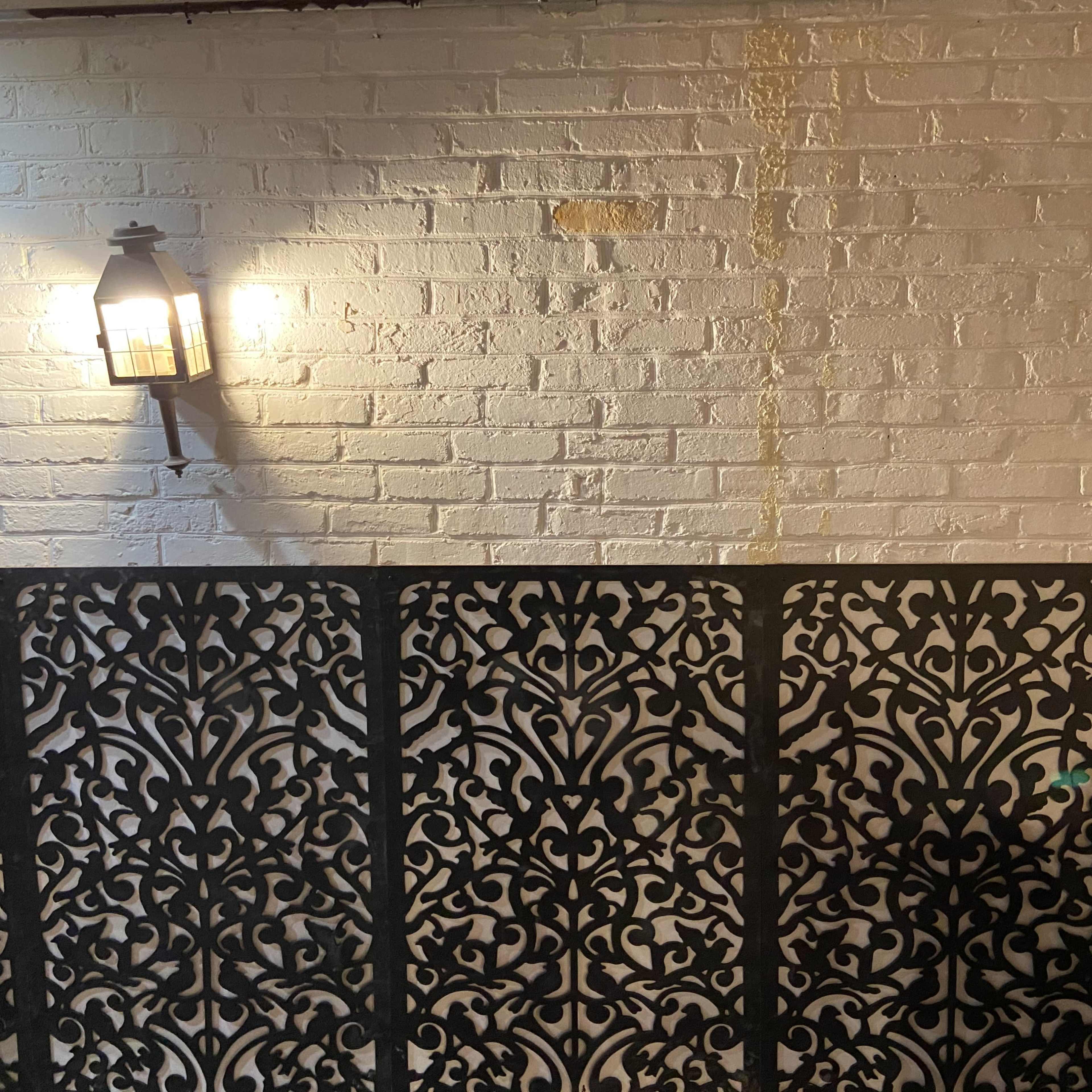 A decorative black screen is positioned in front of a white brick wall illuminated by a wall lantern.