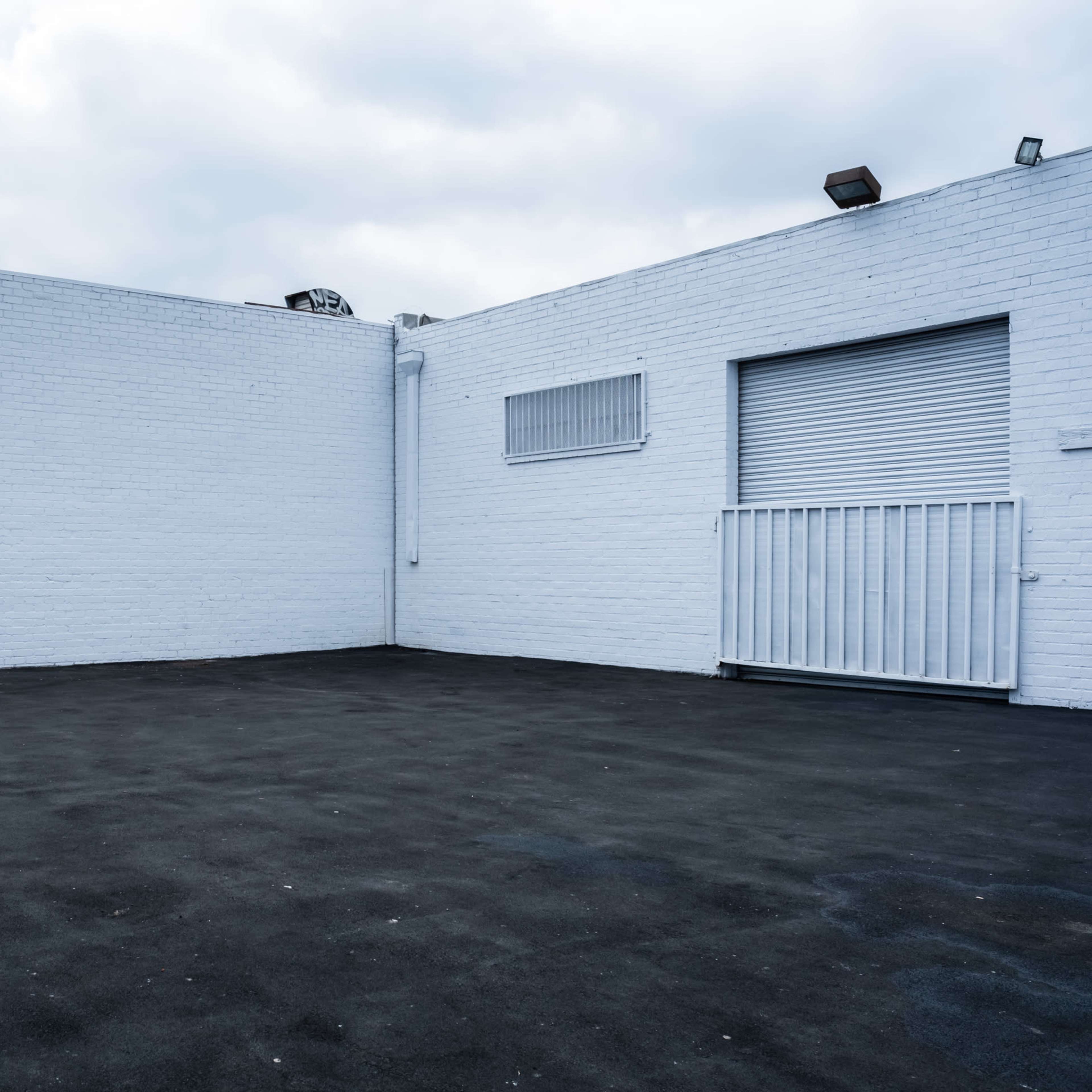 An empty outdoor area with a gray asphalt surface, surrounded by white brick walls and a sign indicating "EXIT."
