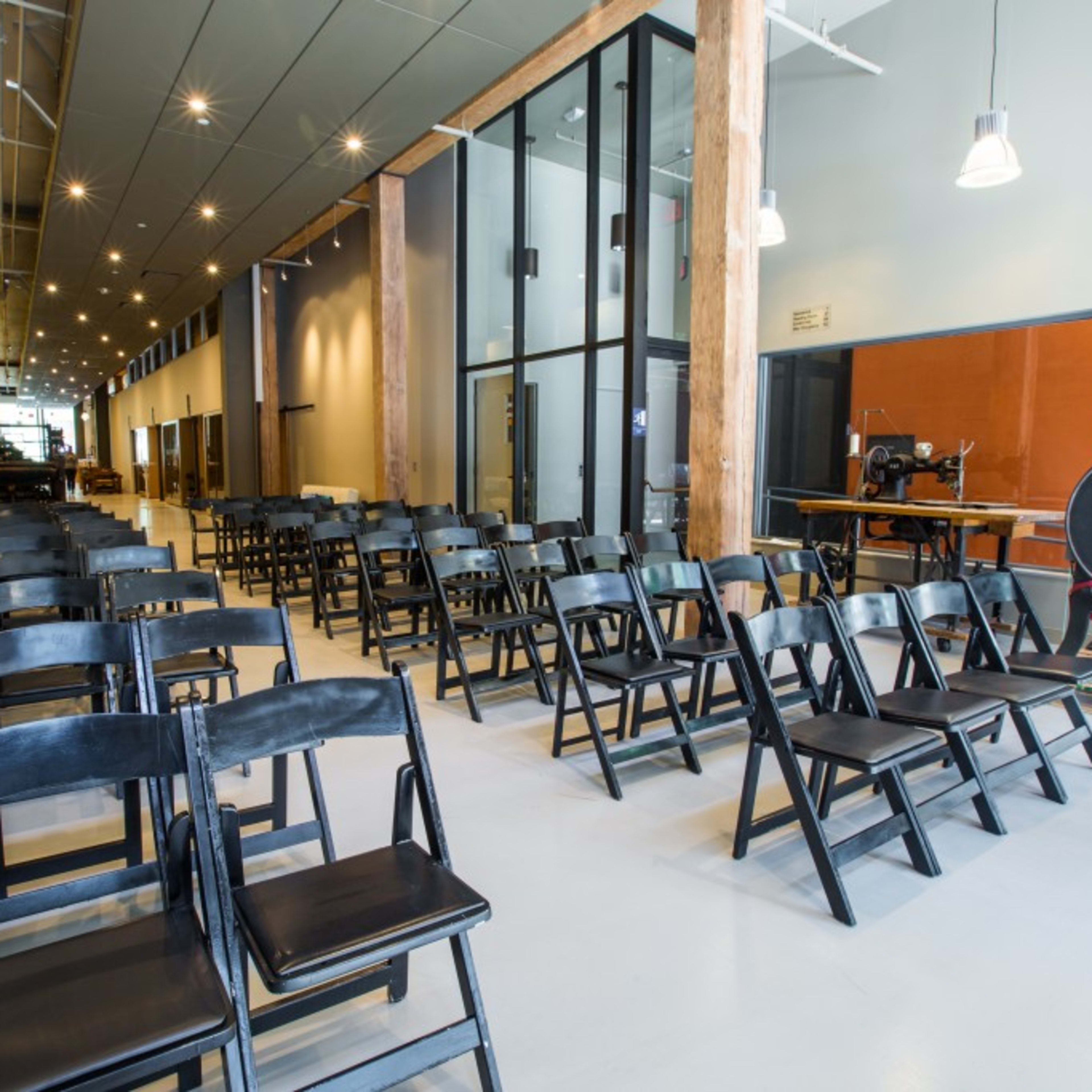 A spacious room with rows of black folding chairs arranged facing a large glass window.