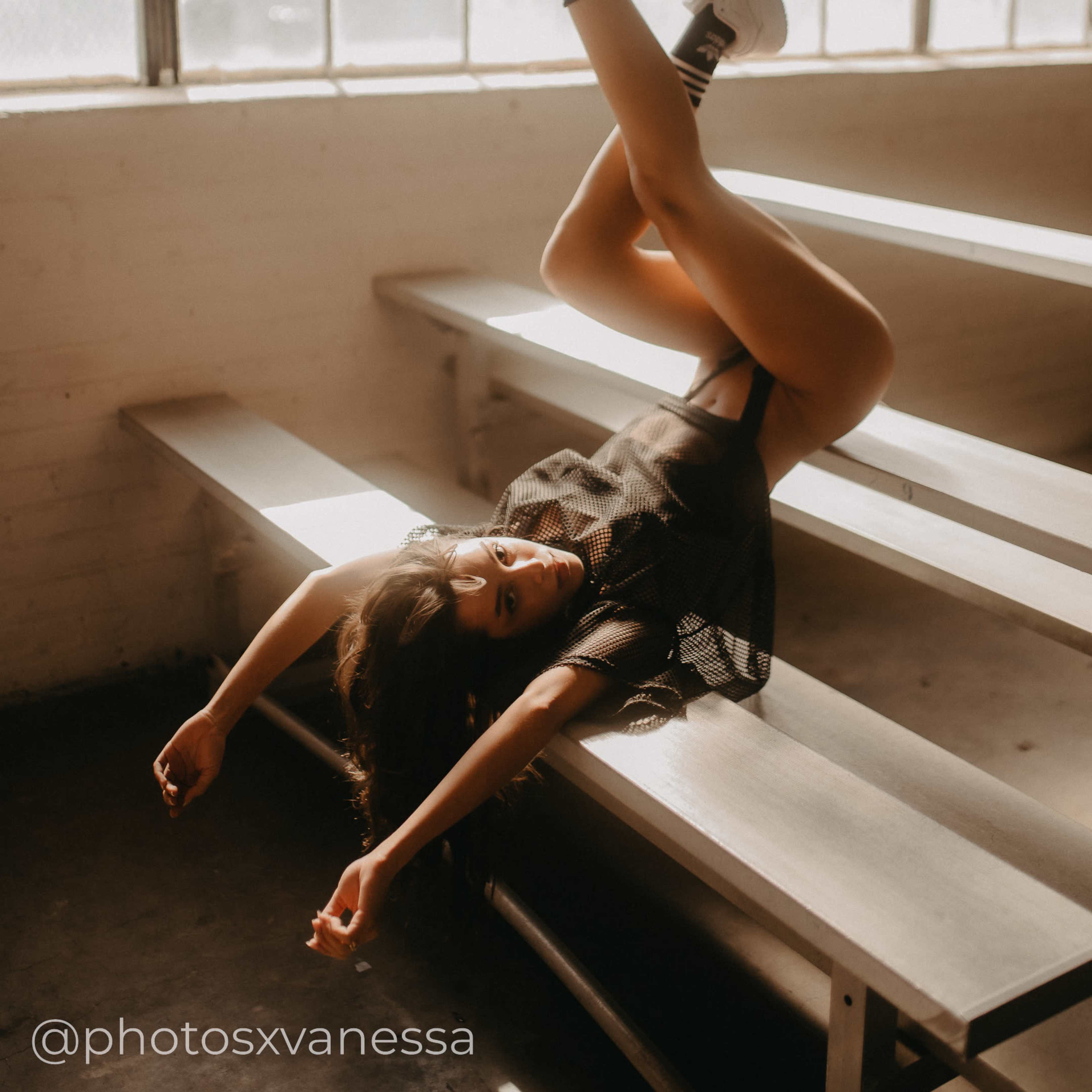 A person is lying on a set of bleachers with one arm raised and legs extended upward.