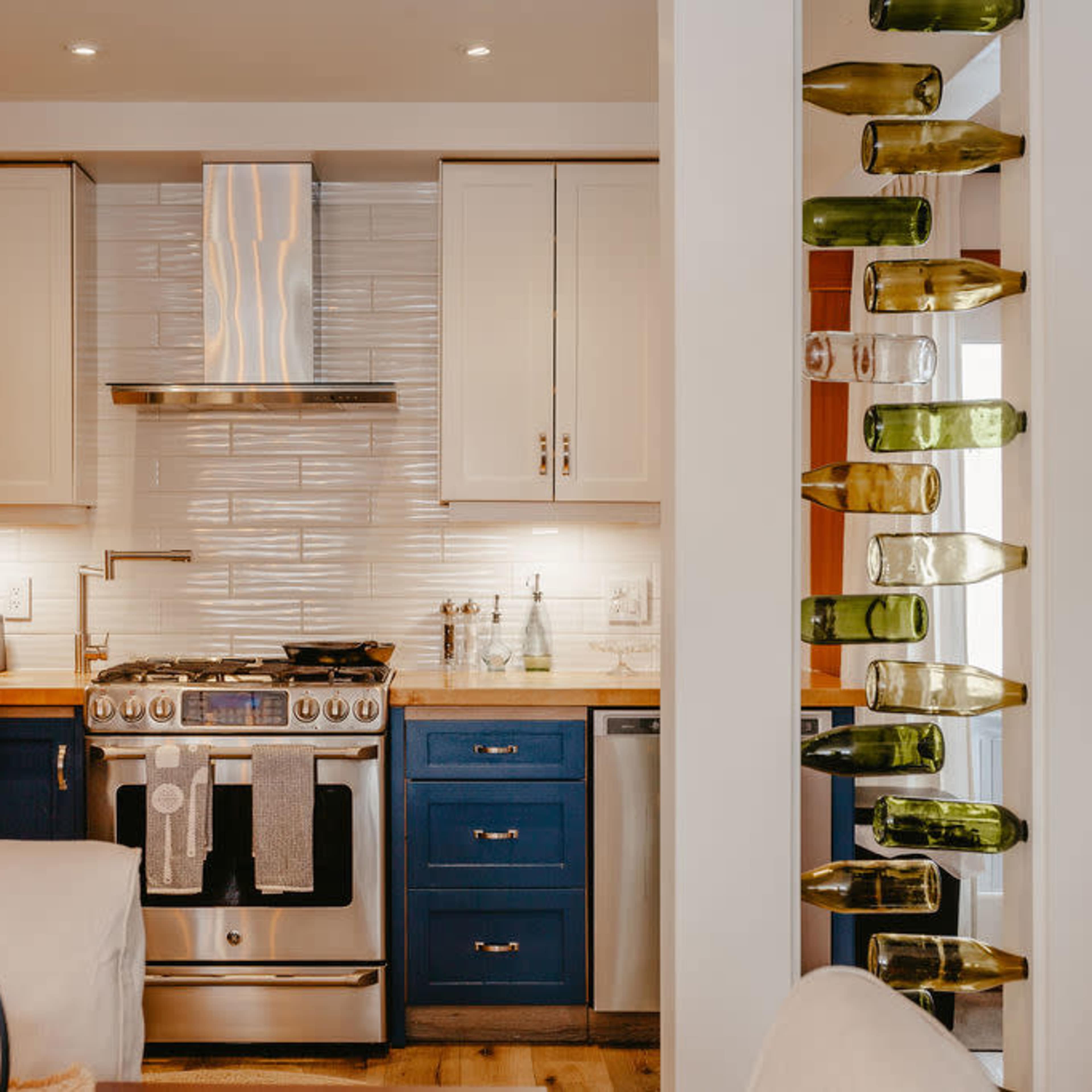 A modern kitchen with sleek cabinets, stainless steel appliances, and a decorative wine bottle display mounted on a column.