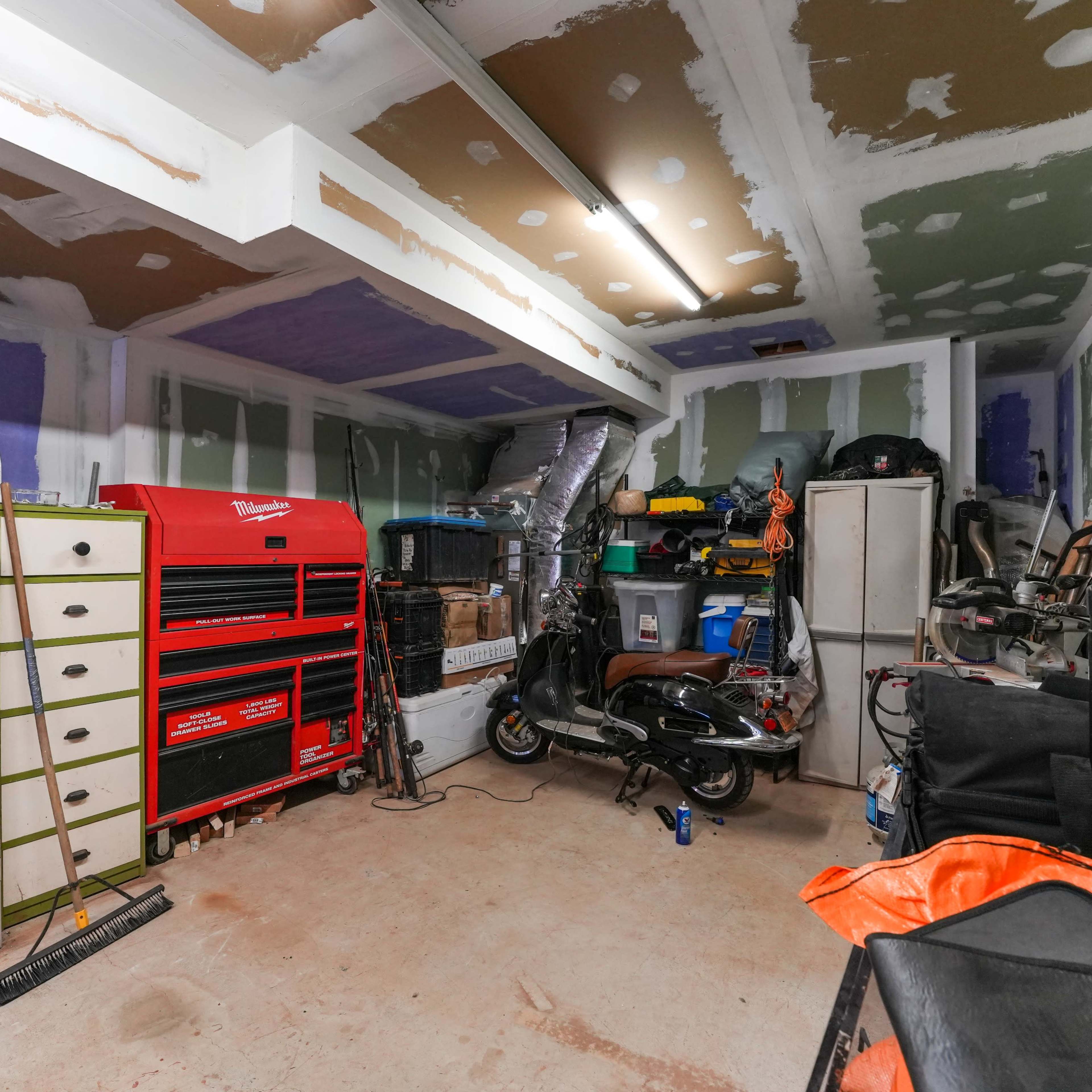 A cluttered garage with various tools, equipment, and storage units arranged along the walls.