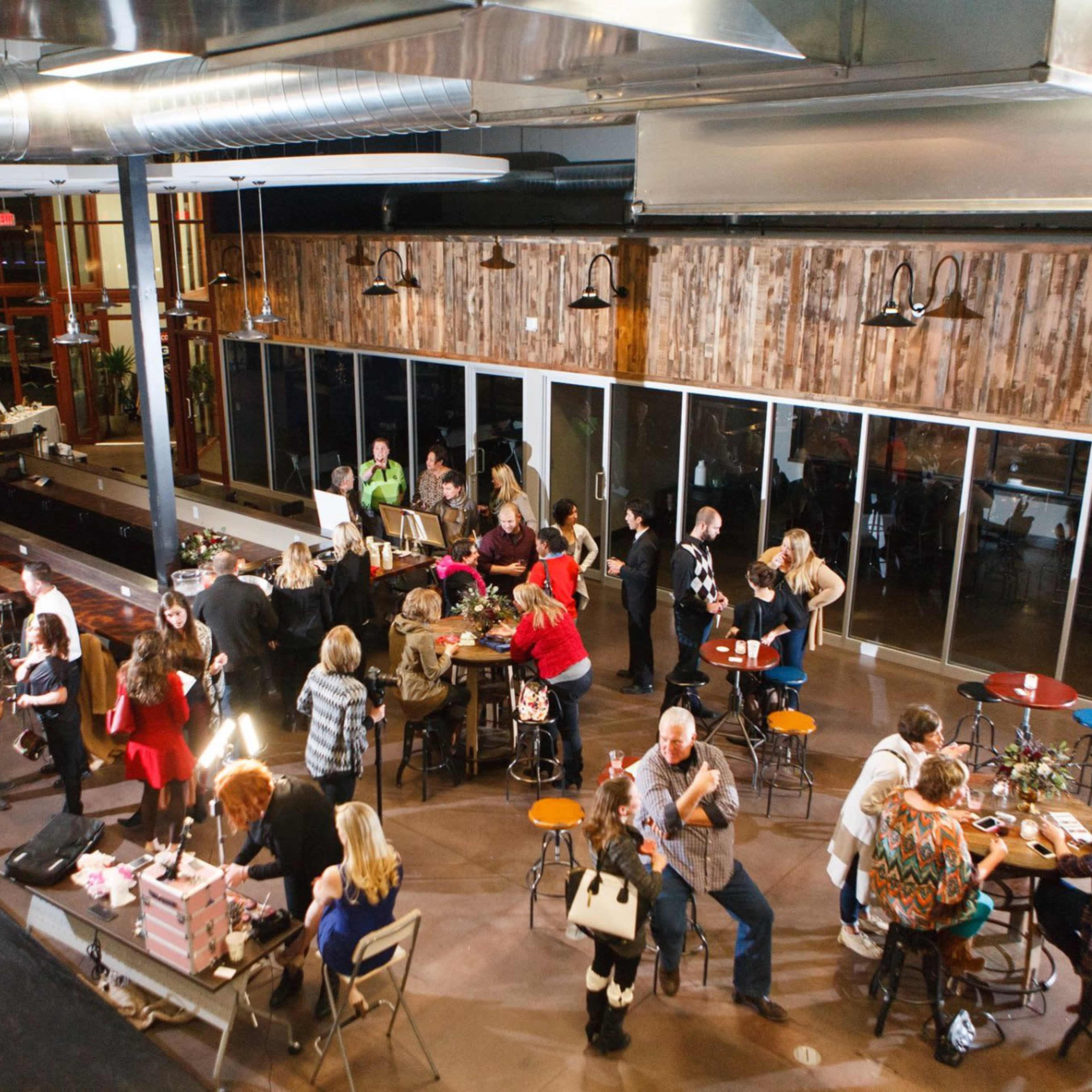 A large group of people gathers in a spacious venue with wooden walls and festive decorations, engaging in various activities around tables.