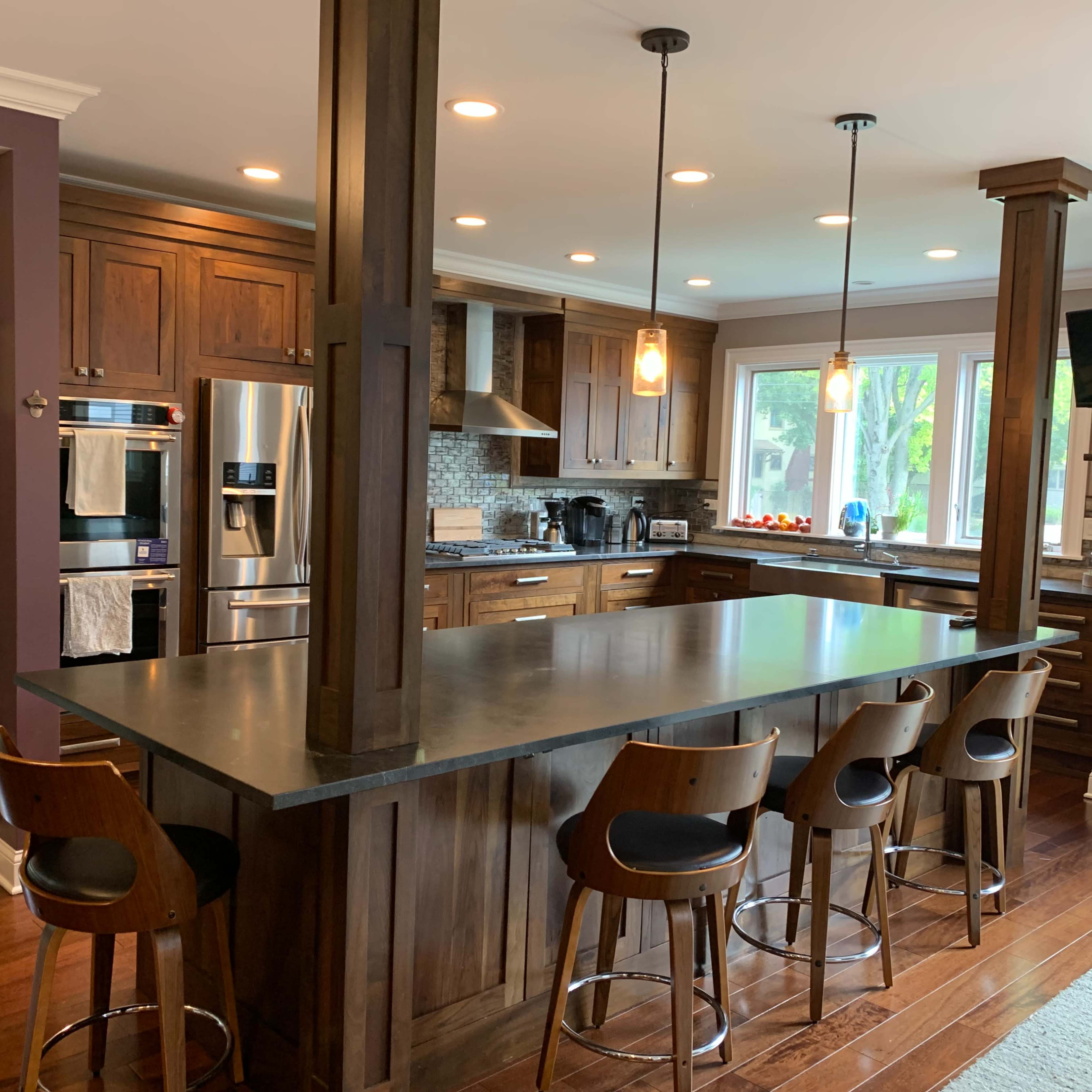 A modern kitchen with wooden cabinetry, a large island with seating for four, and stainless steel appliances.