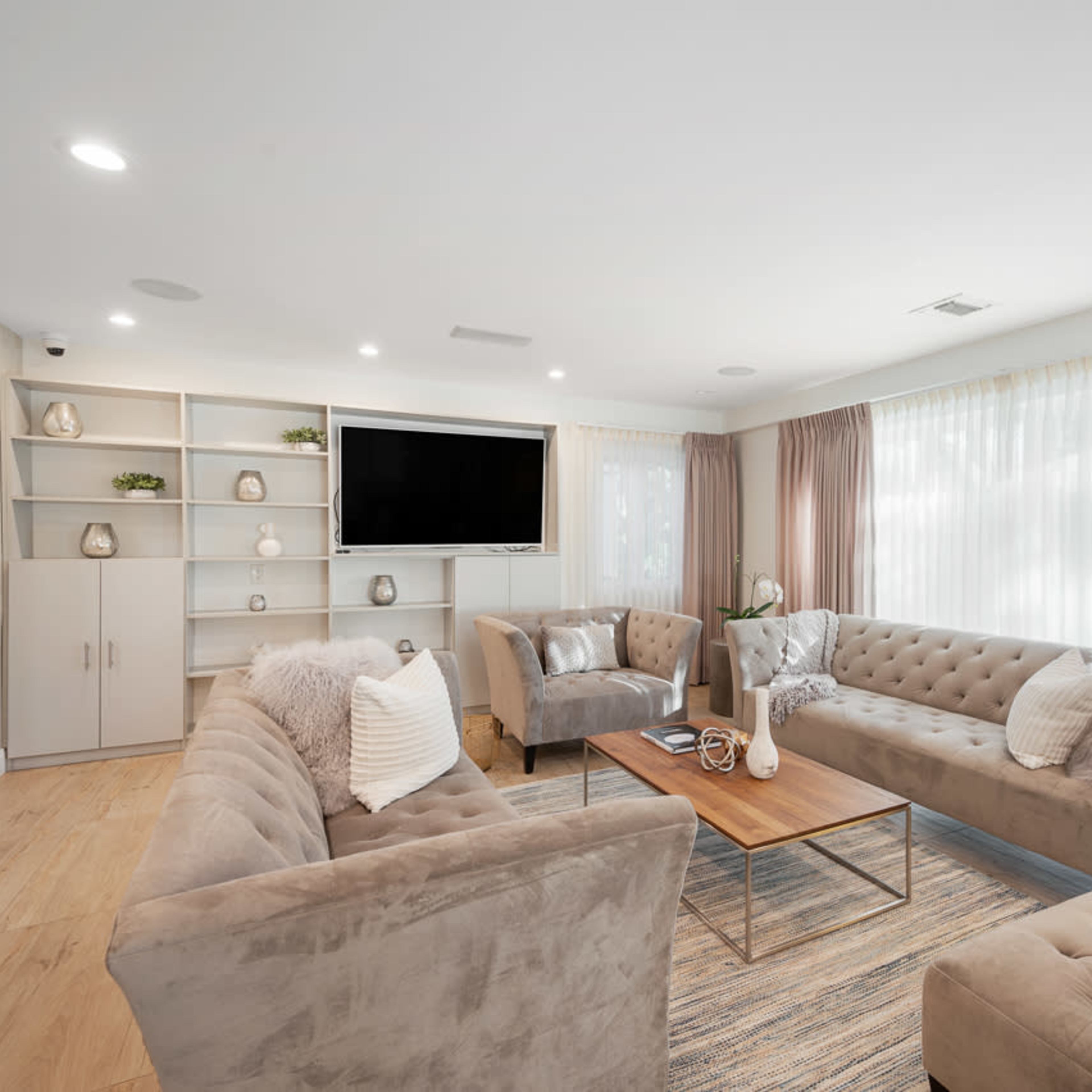 The living room features a neutral color scheme with two plush sofas, a wooden coffee table, and a large television mounted on a wall unit.