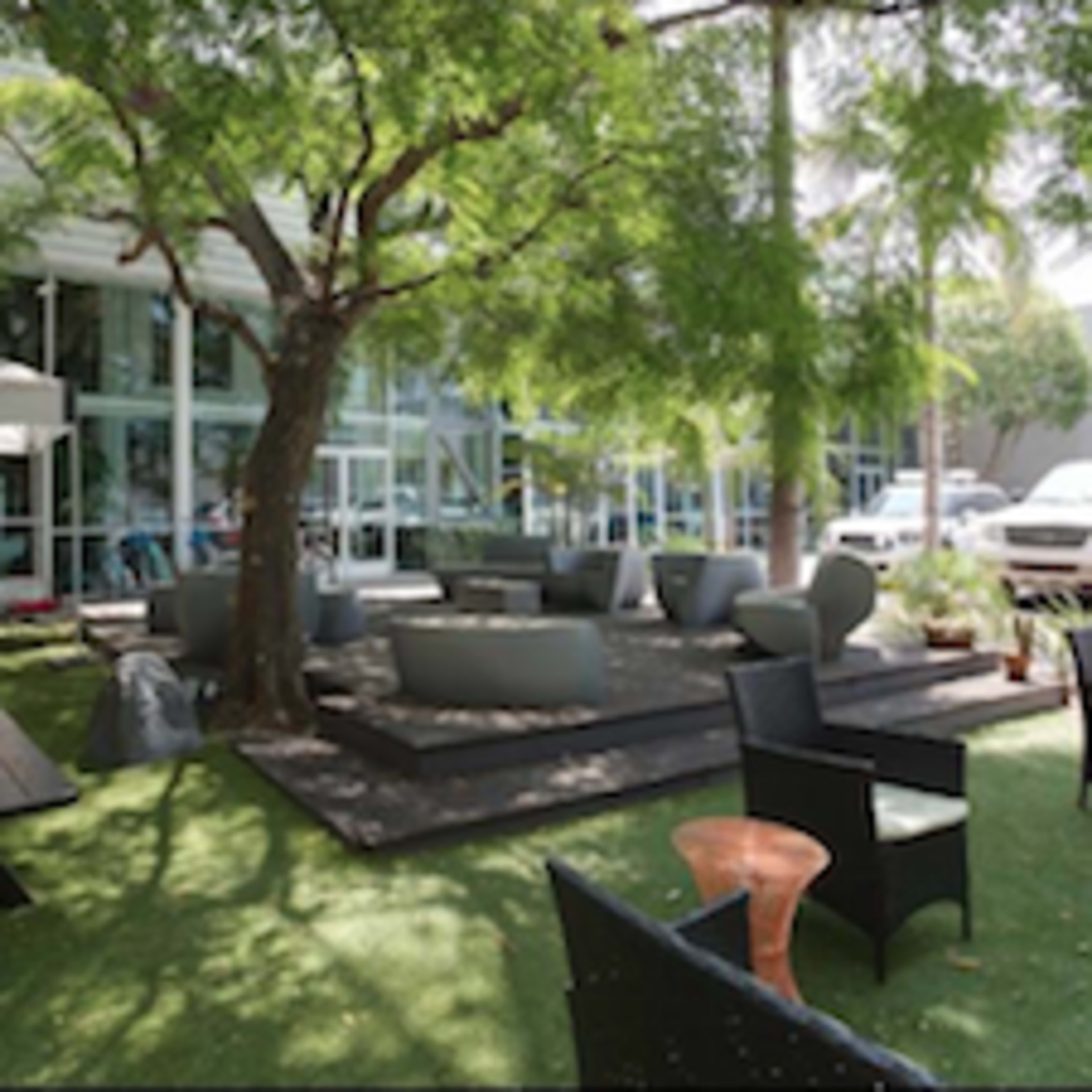 A landscaped outdoor seating area with tables, chairs, and a large tree beside a modern building.