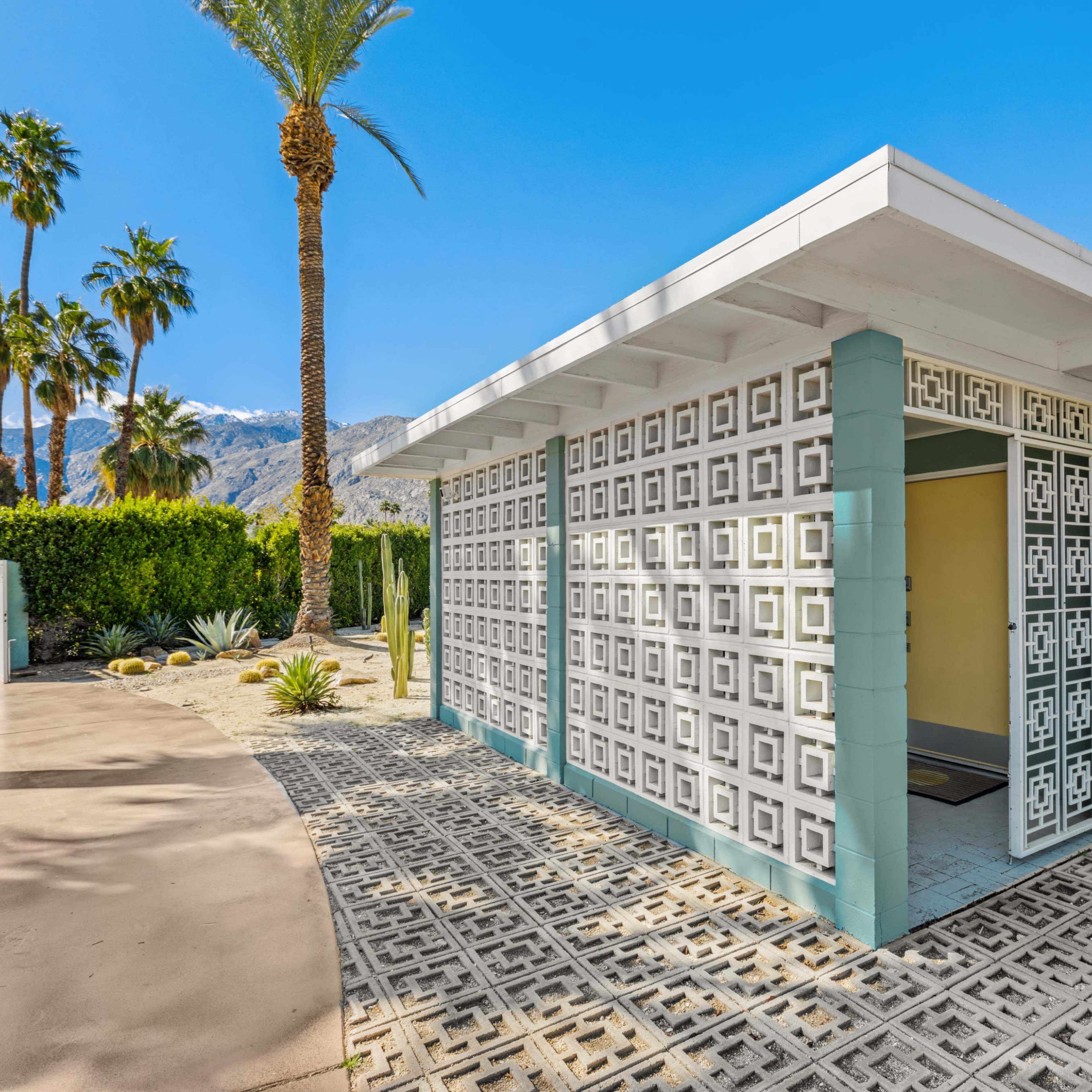 A modern house entrance with patterned concrete walls and palm trees in the background.