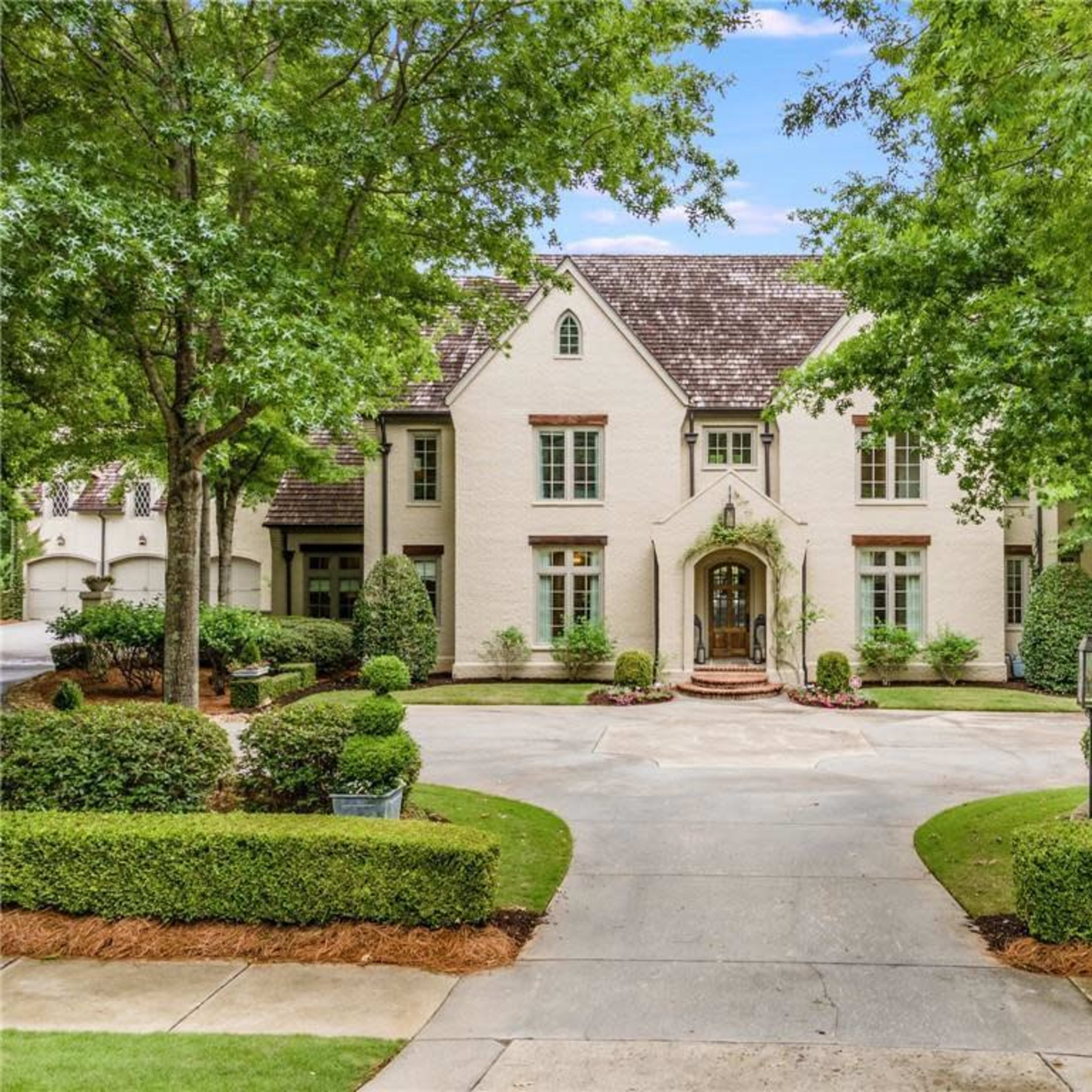 A large, two-story white house surrounded by neatly trimmed greenery and a circular driveway.