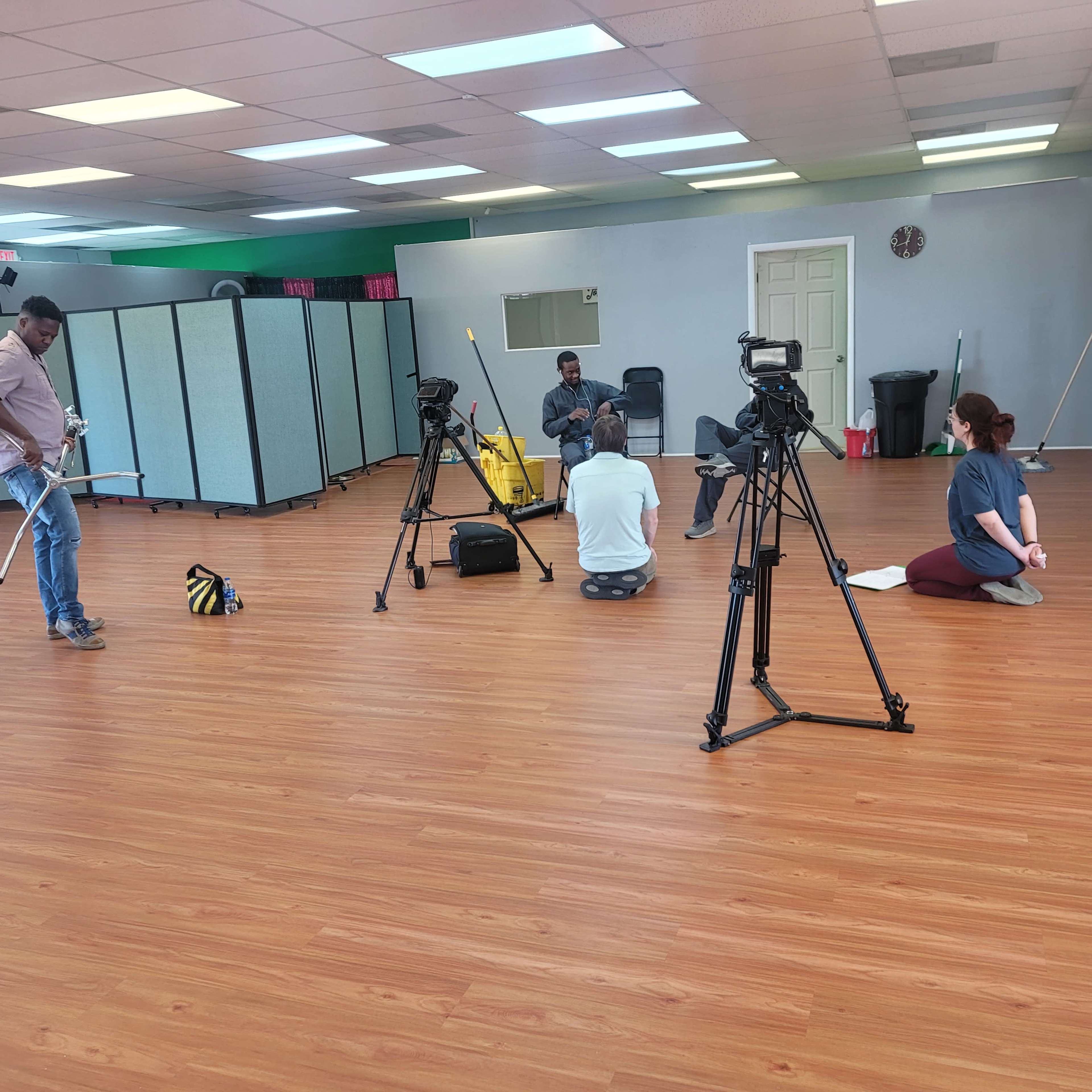 A group of people are practicing dance in a spacious studio with hardwood floors and large mirrors.