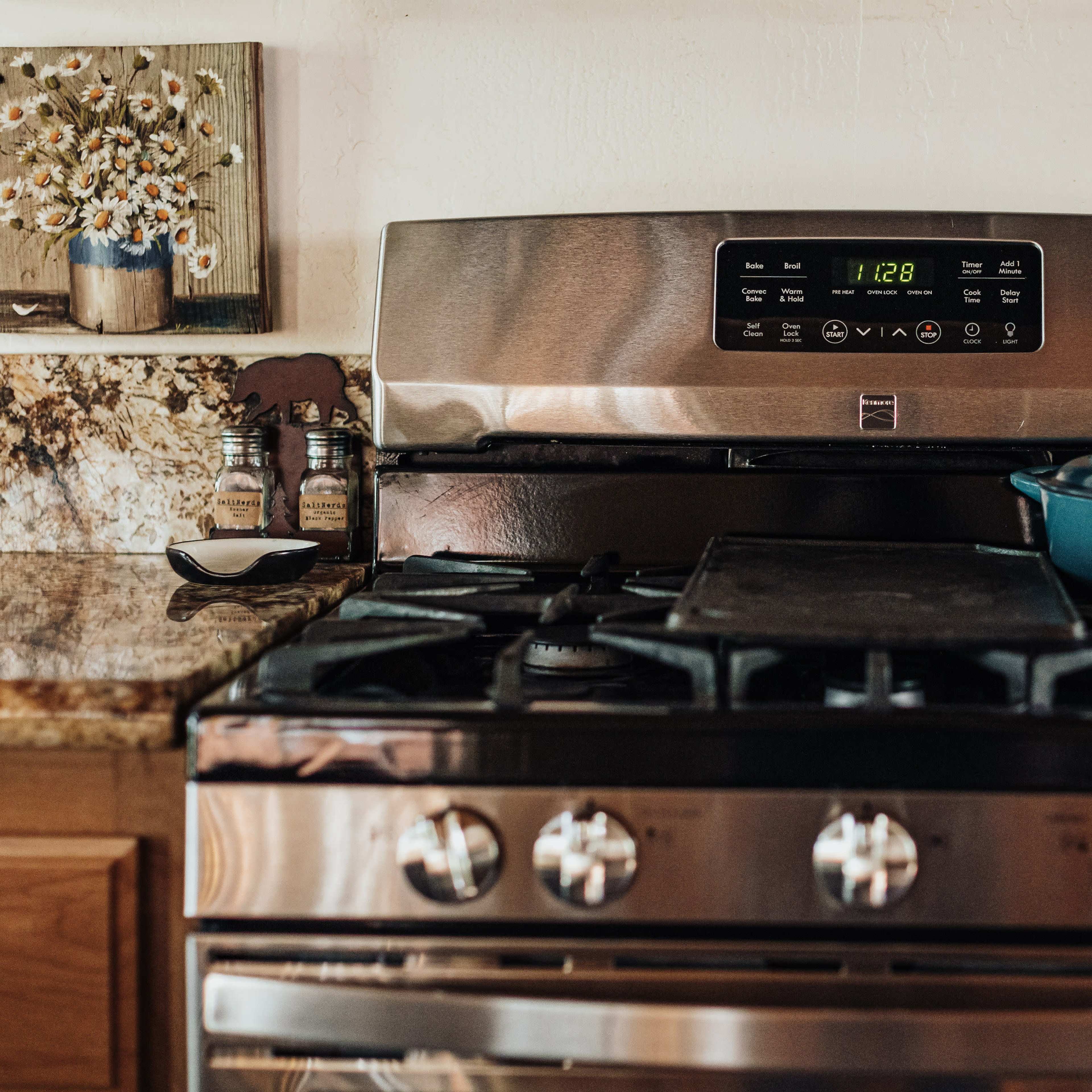 A stainless steel gas stove with a blue pot on top and a digital display shows the time.