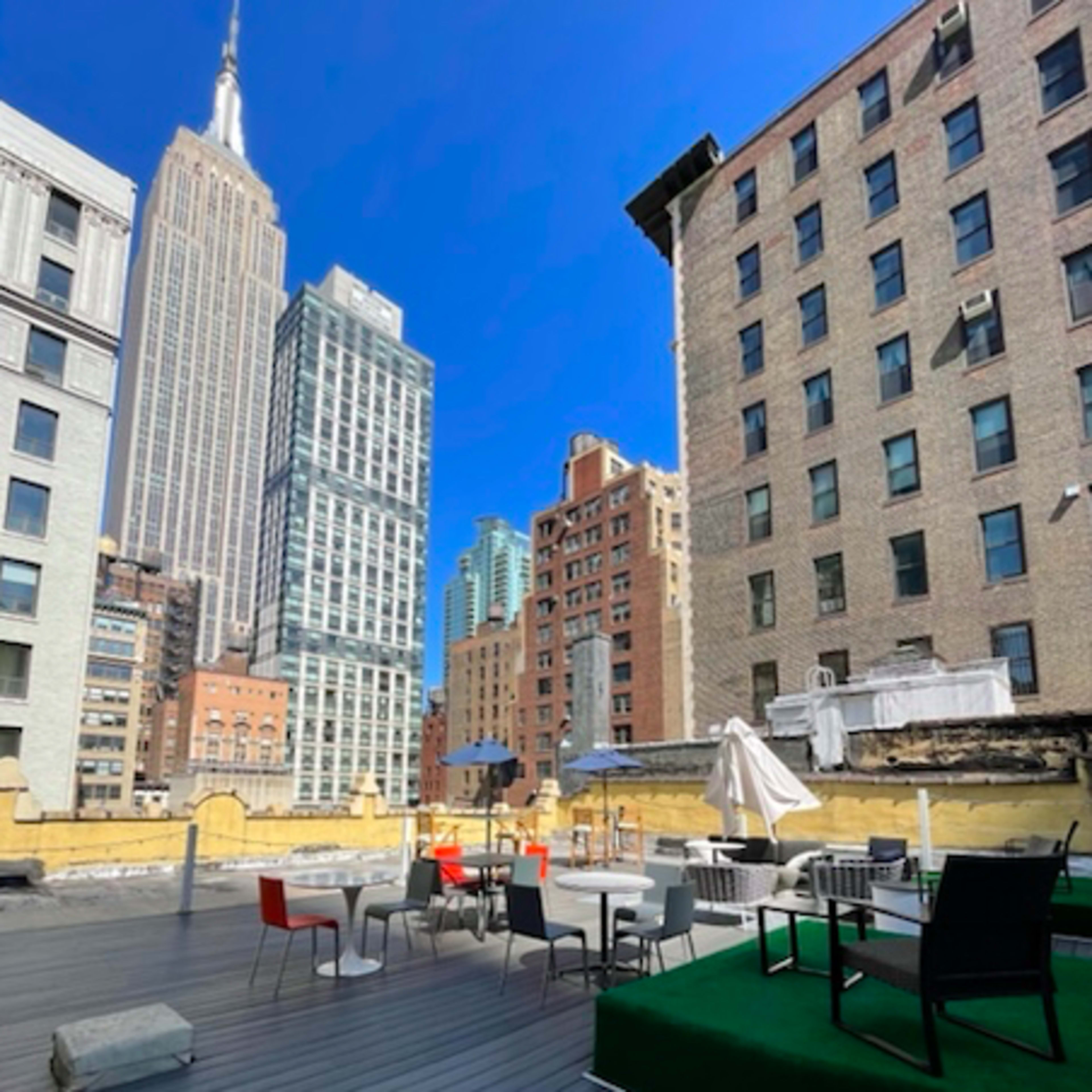 A rooftop patio features modern seating and greenery with the Empire State Building visible in the background.