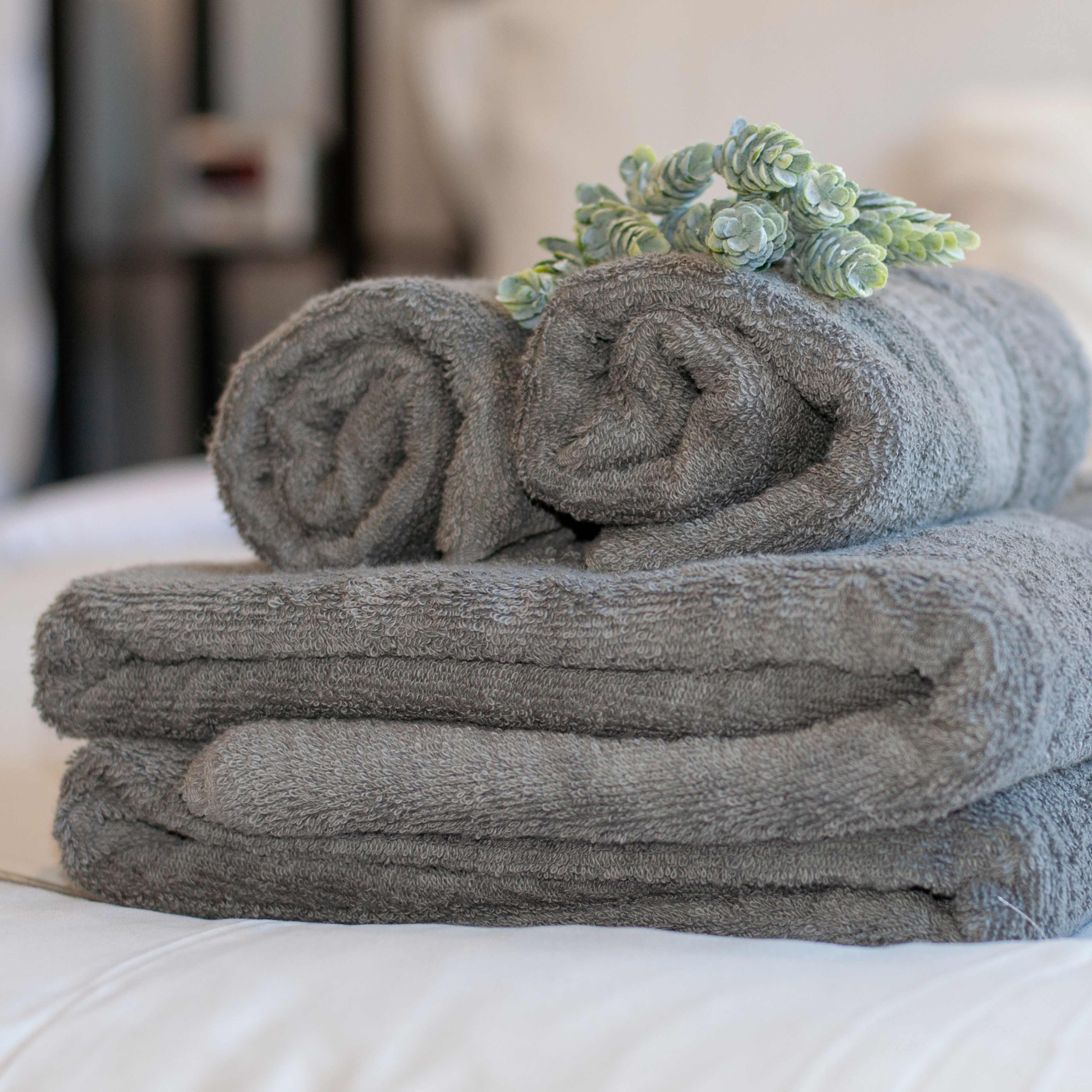 A stack of rolled and folded gray towels is placed on a bed with a small decorative plant on top.