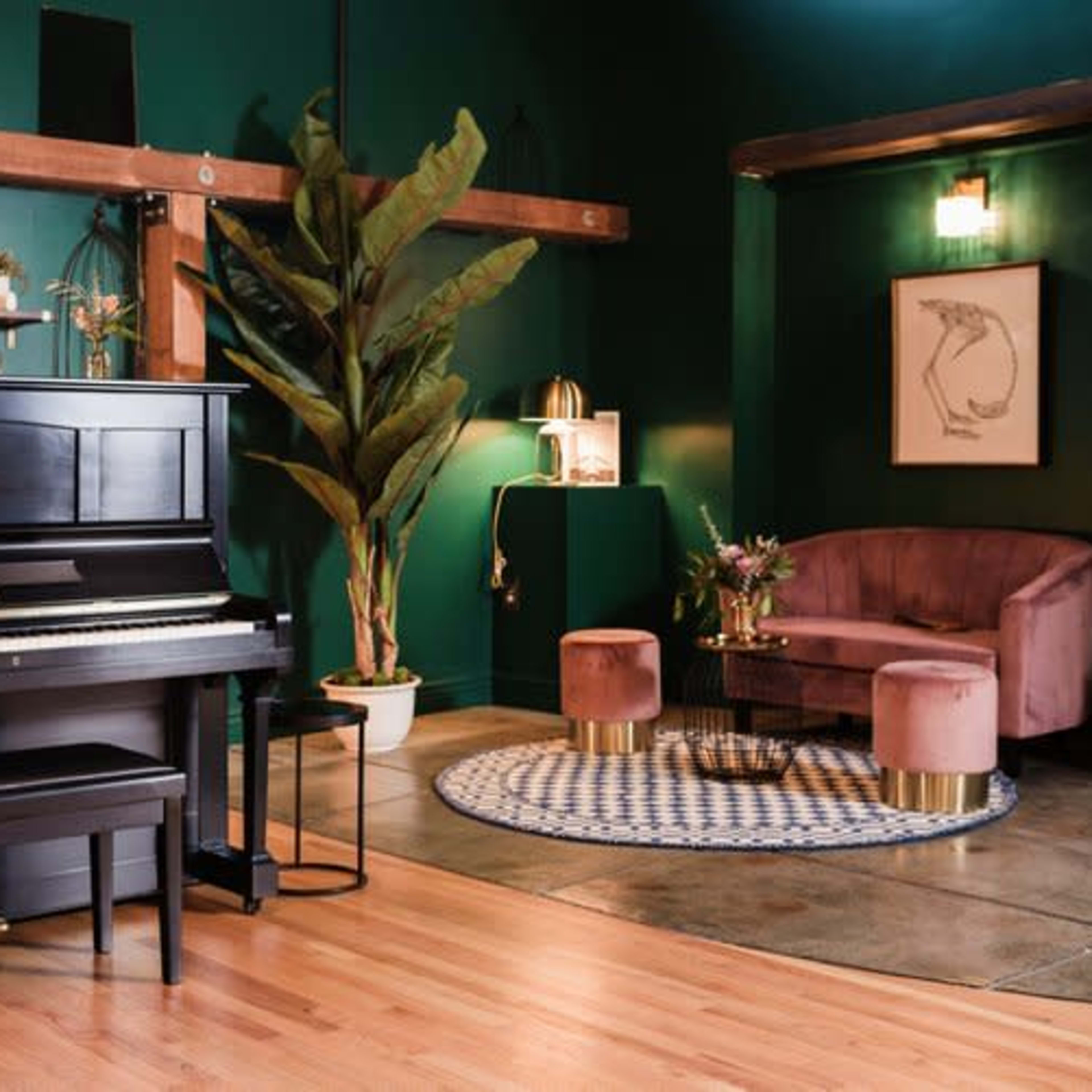 A black upright piano sits beside a plush purple seating area in a room with dark green walls and wooden beams.
