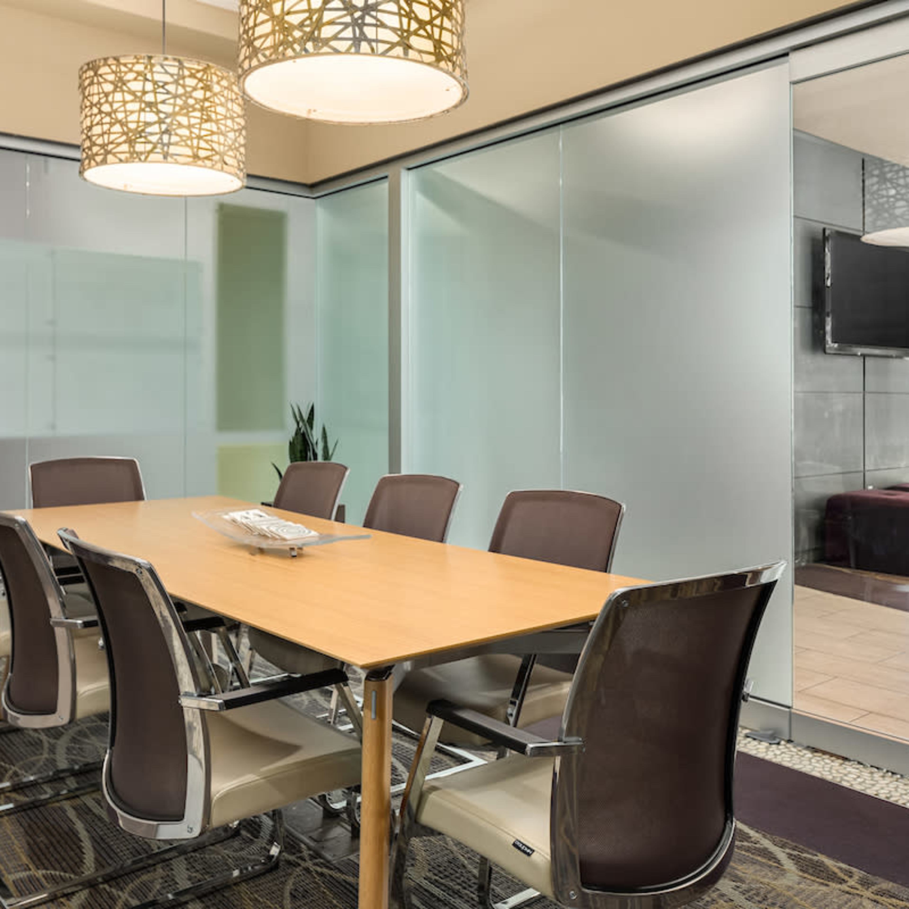A modern conference room with a wooden table surrounded by six chairs, glass walls, and pendant lighting.