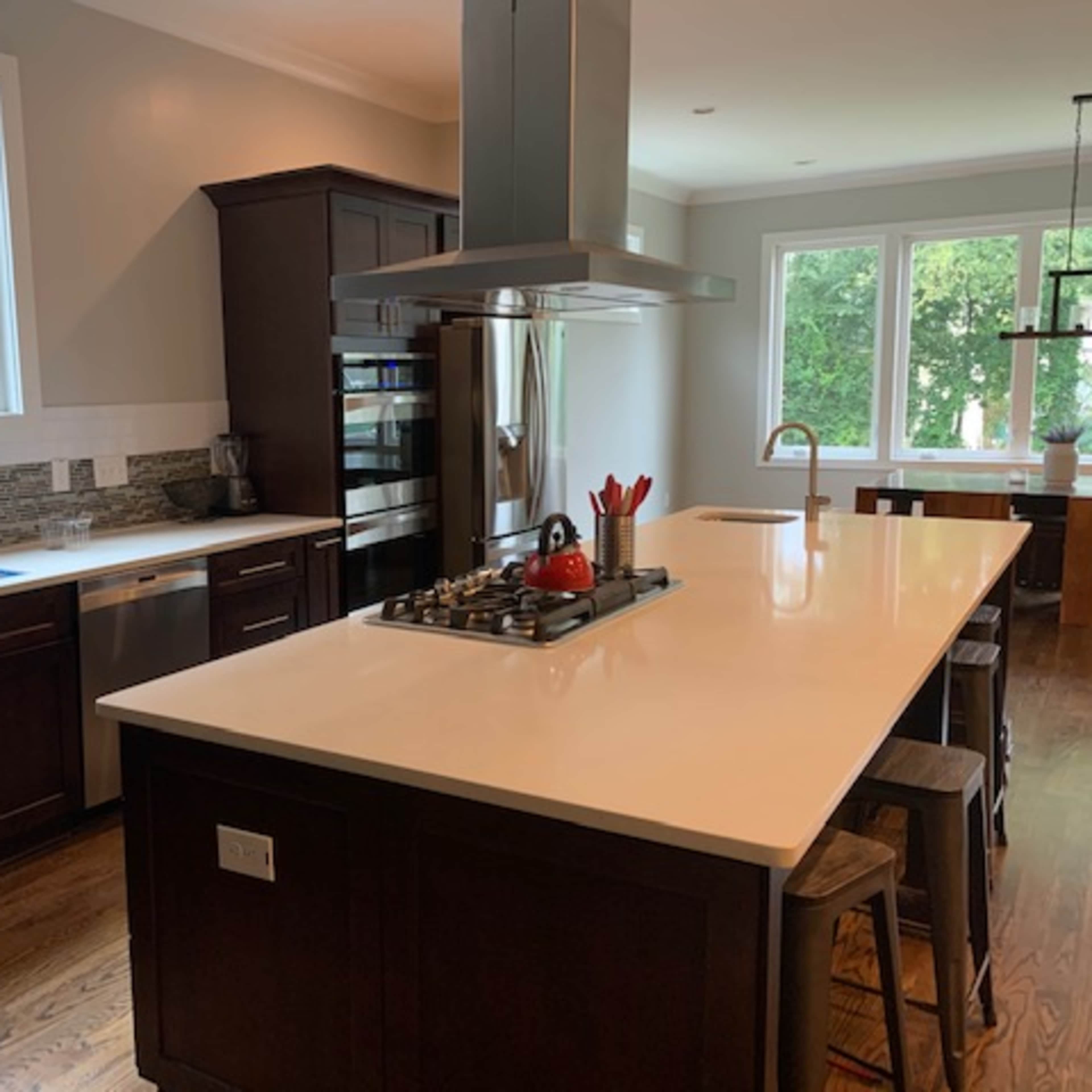 A modern kitchen featuring dark wood cabinetry, a central island with a white countertop, and stainless steel appliances.