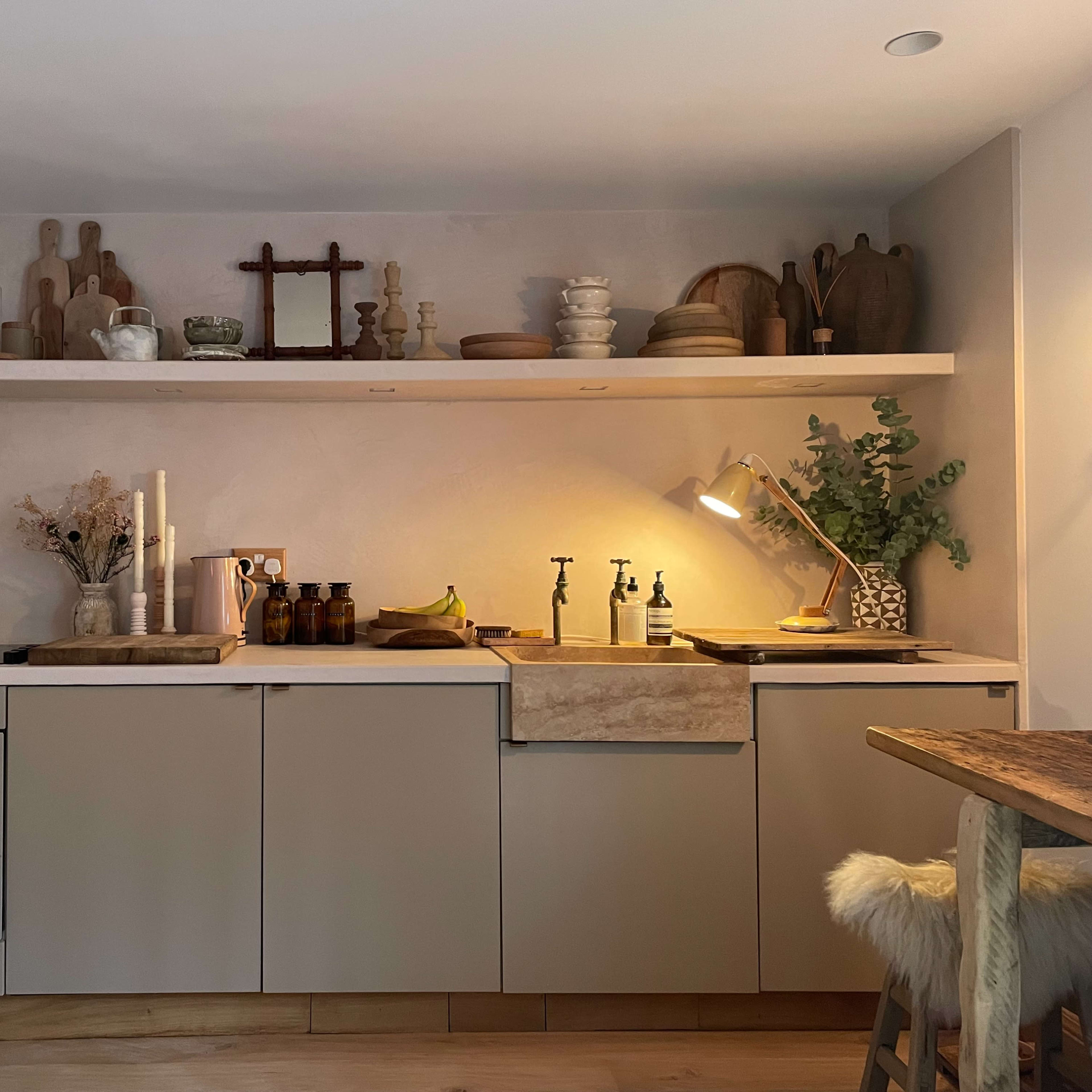 A modern kitchen features a minimalist design with a countertop, sink, and various utensils and decorative items arranged on shelves above.