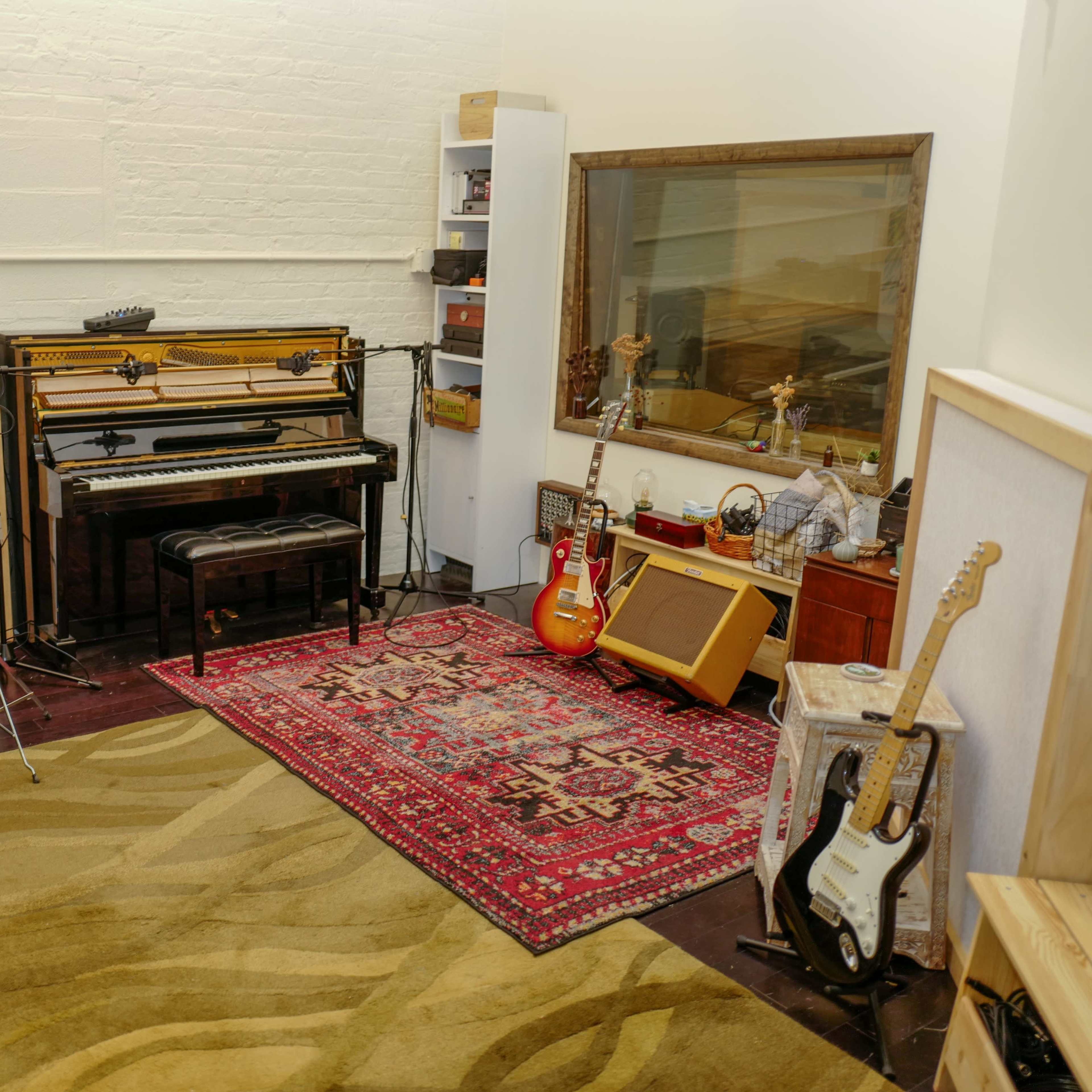 A music studio features a drum set, a piano, electric guitars, and various music equipment arranged on a carpet with a decorative rug.