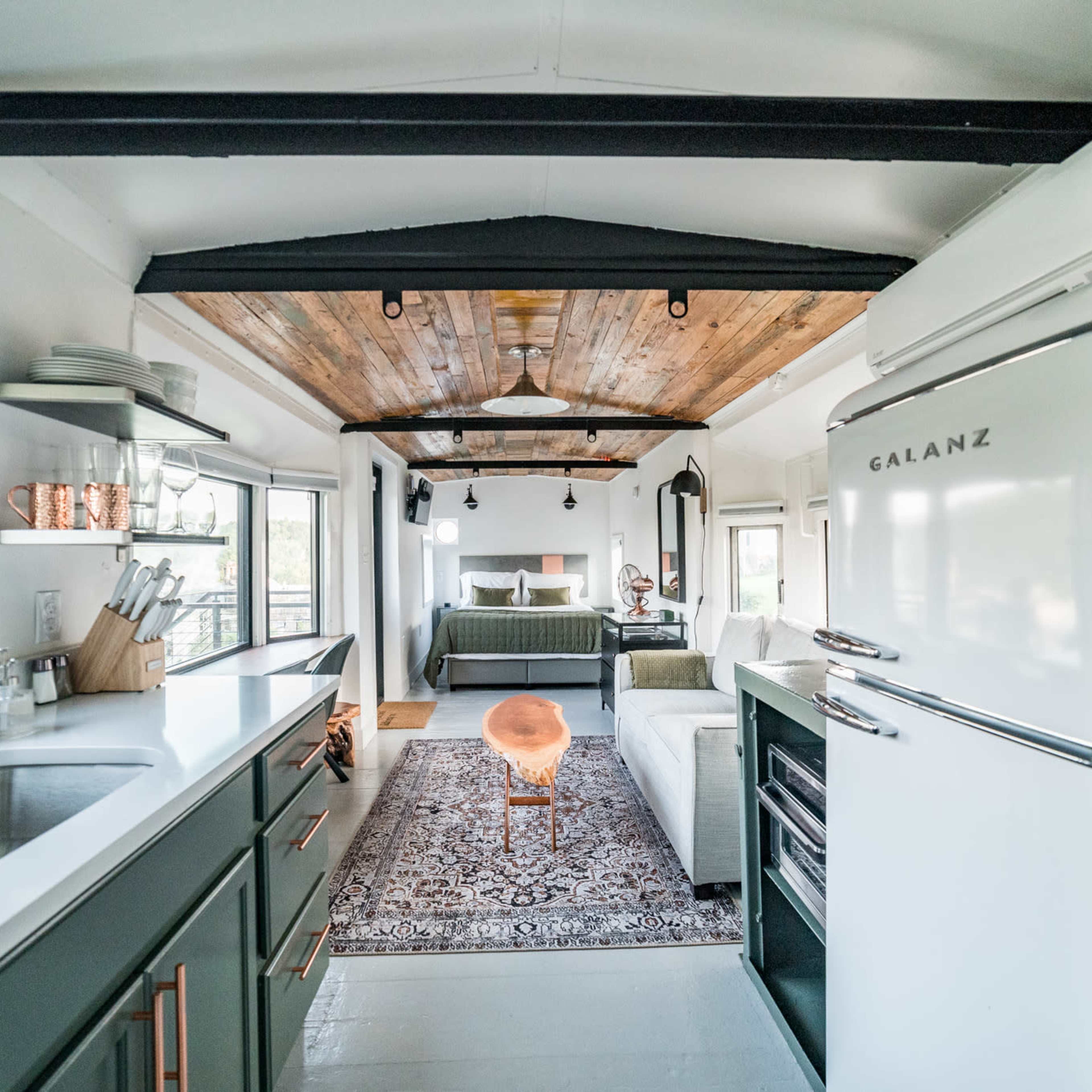 A compact kitchen and living area feature a wood-paneled ceiling, modern appliances, and a cozy seating arrangement.