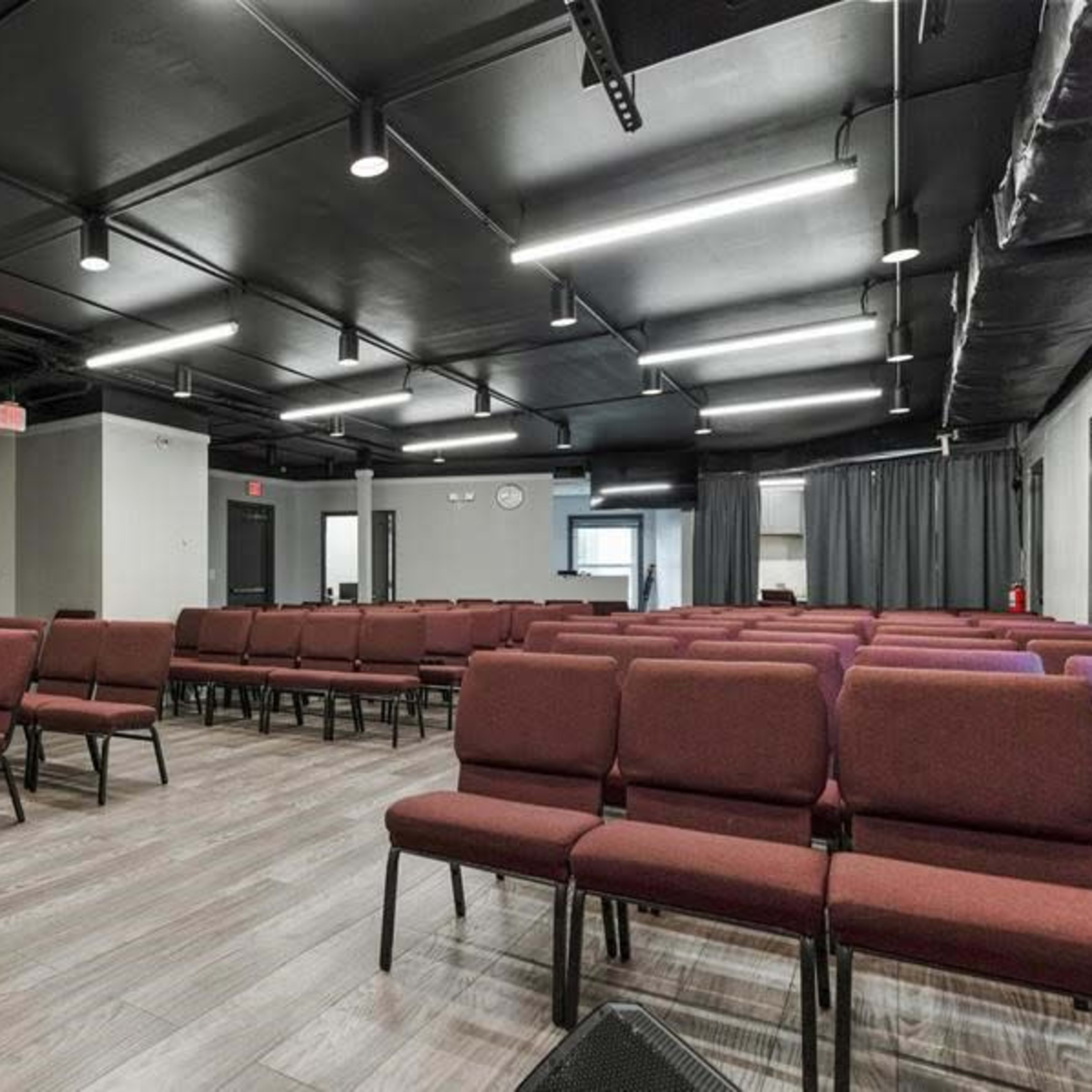 A spacious meeting room features rows of maroon chairs and a small platform at the front.
