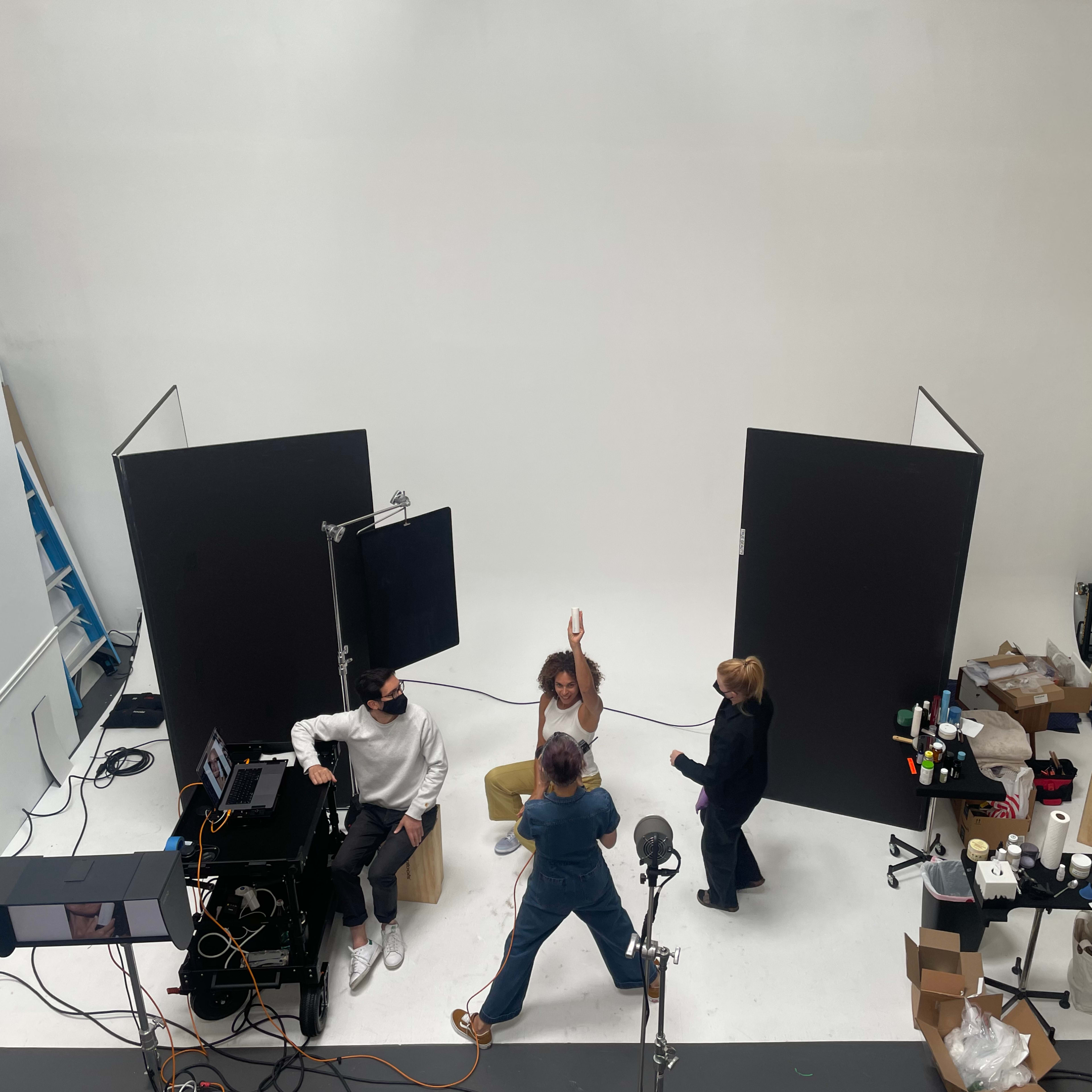A group of four people are engaged in a photography session in a studio with a plain white backdrop and various equipment scattered around.