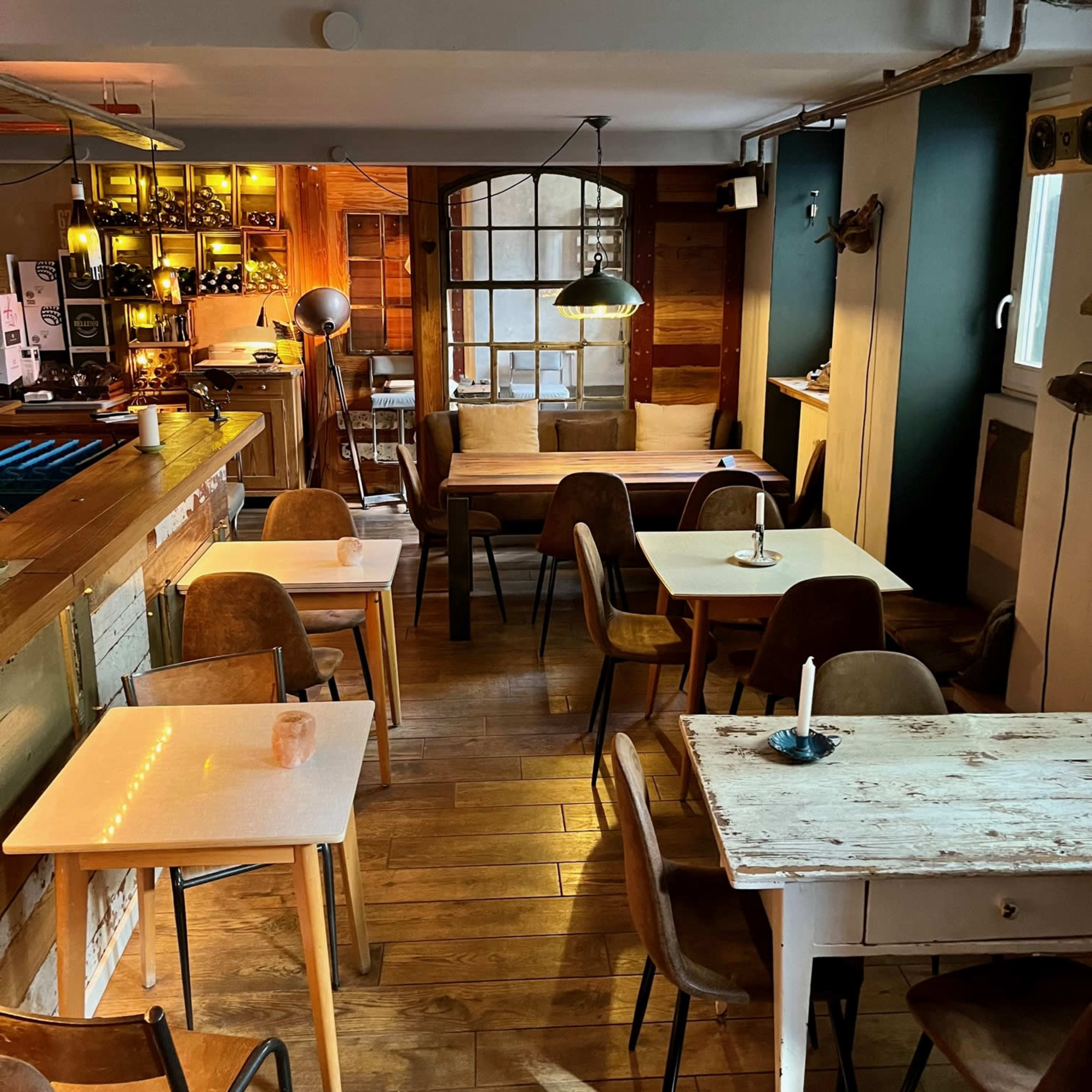 A cozy café interior with wooden floors, various tables, and warm lighting.