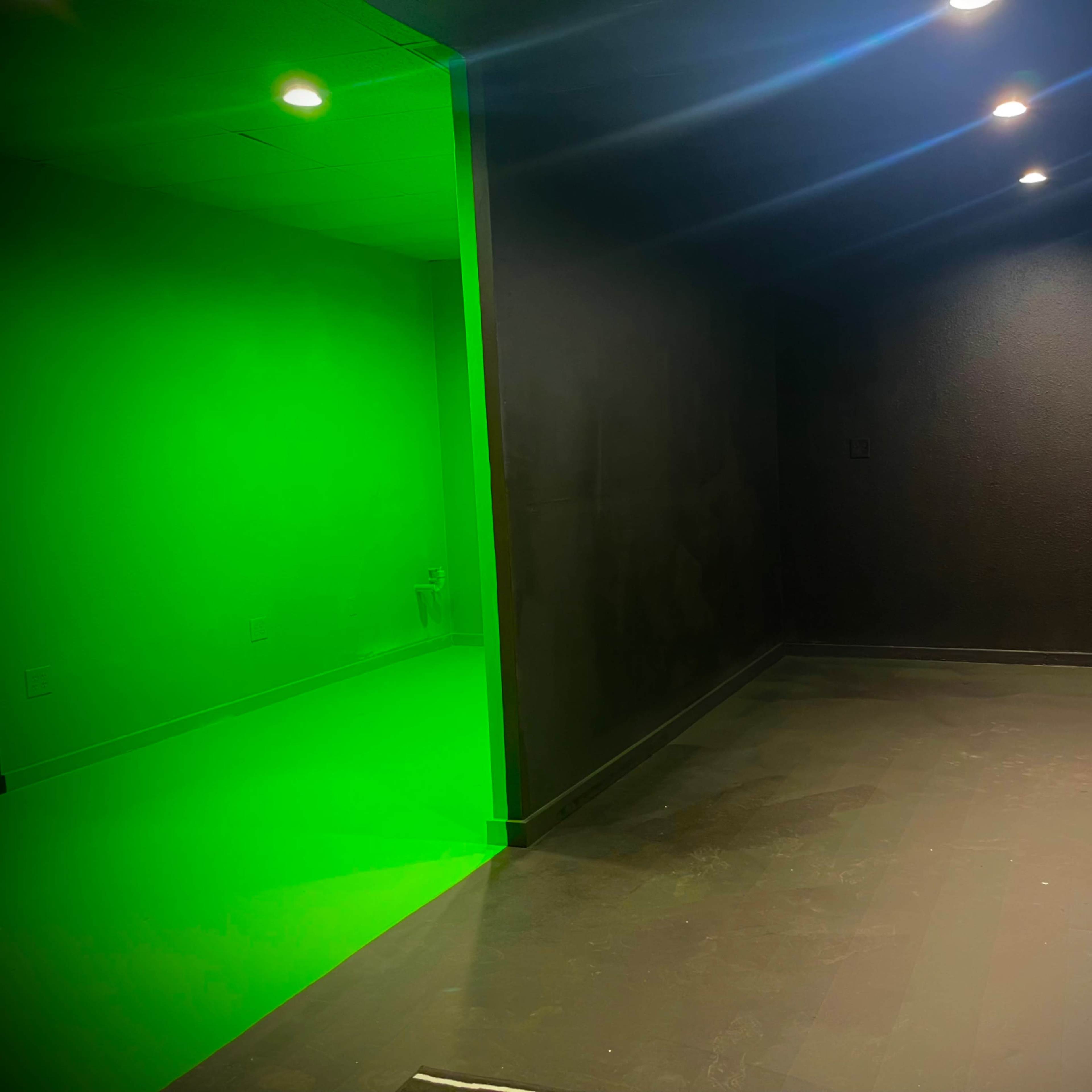 A dimly lit room with black walls and a brightly illuminated green section on one side.