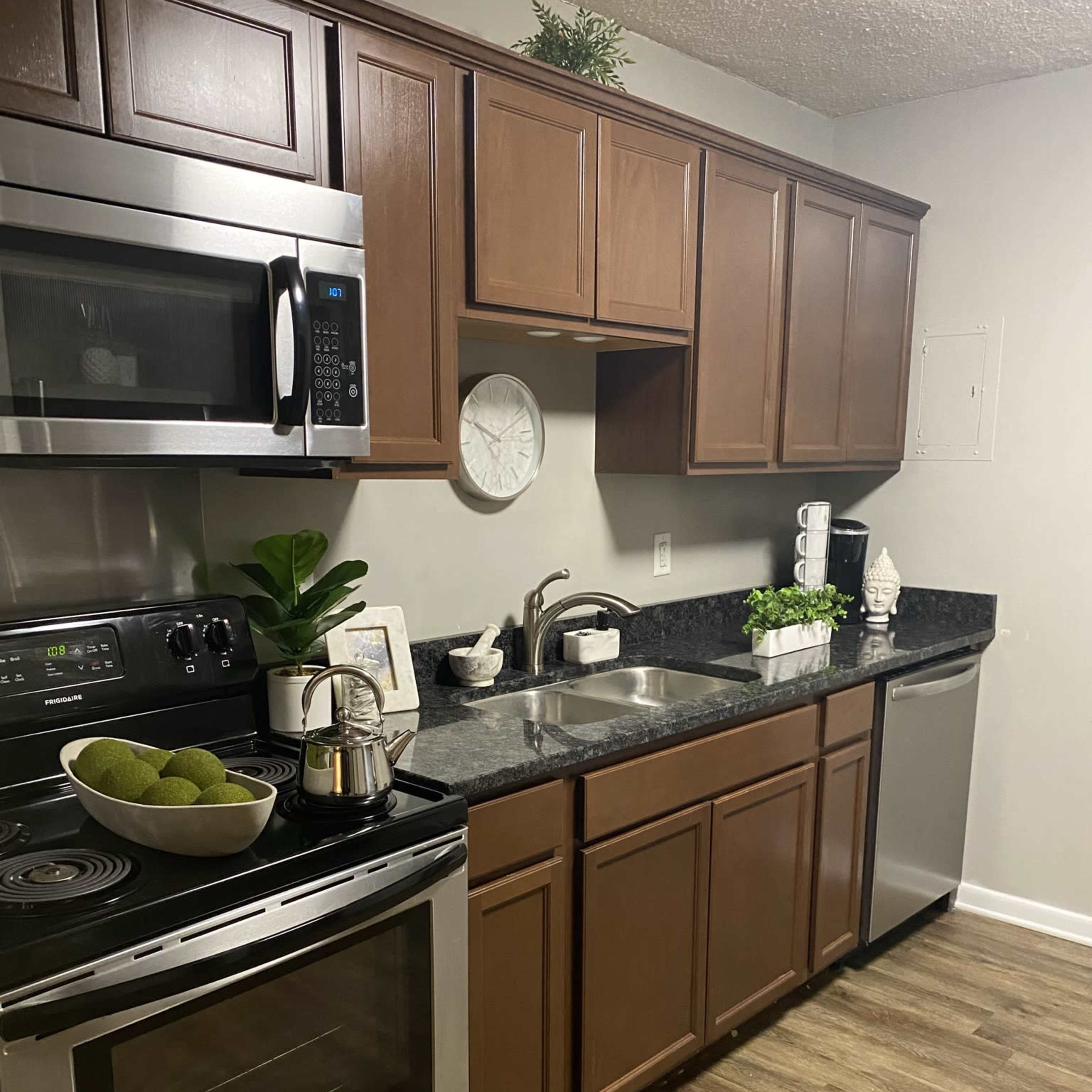 A modern kitchen with dark wood cabinets, stainless steel appliances, a granite countertop, and an organized arrangement of decorative plants.