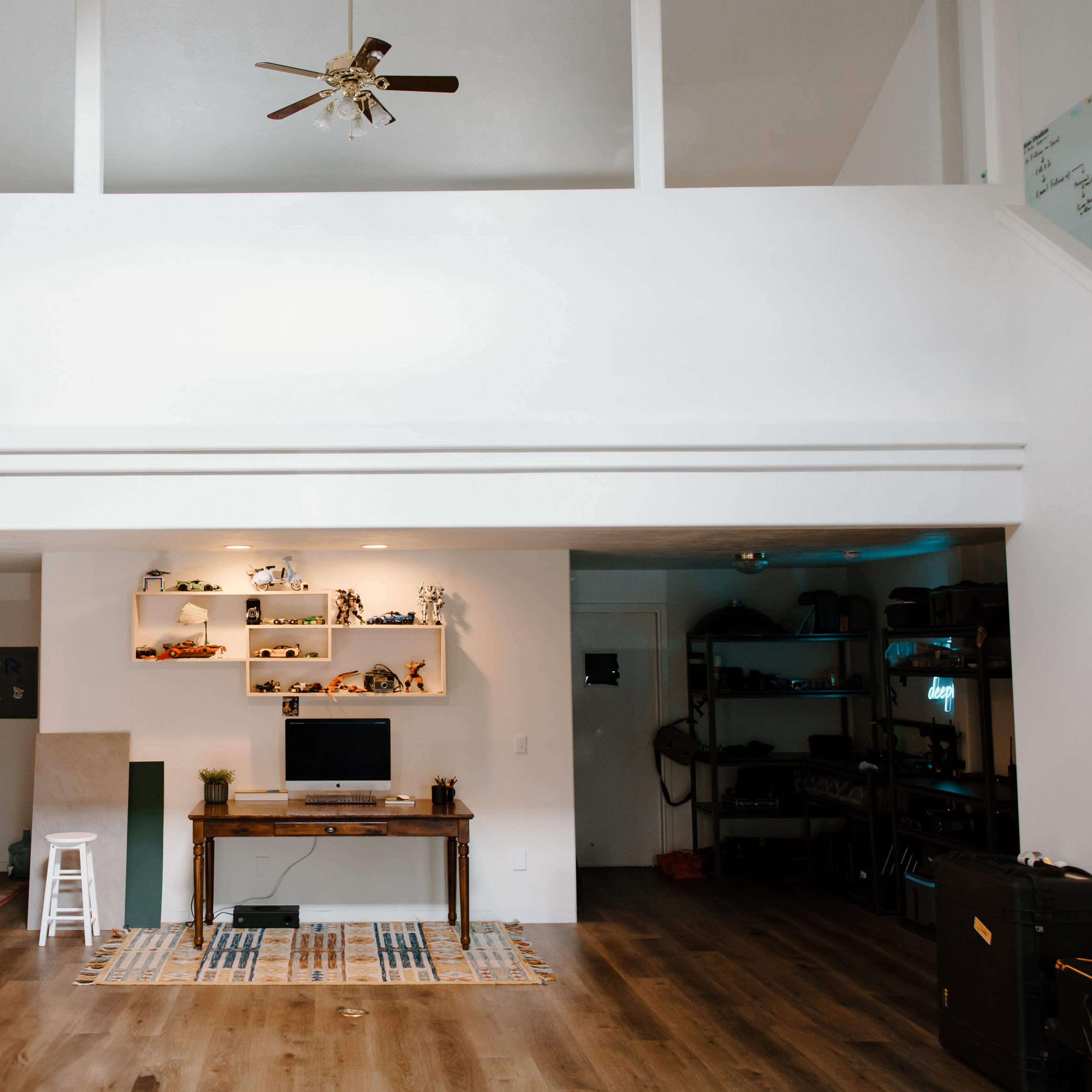 A spacious, open-concept living area with a kitchen, a work desk, and shelves displaying various objects.