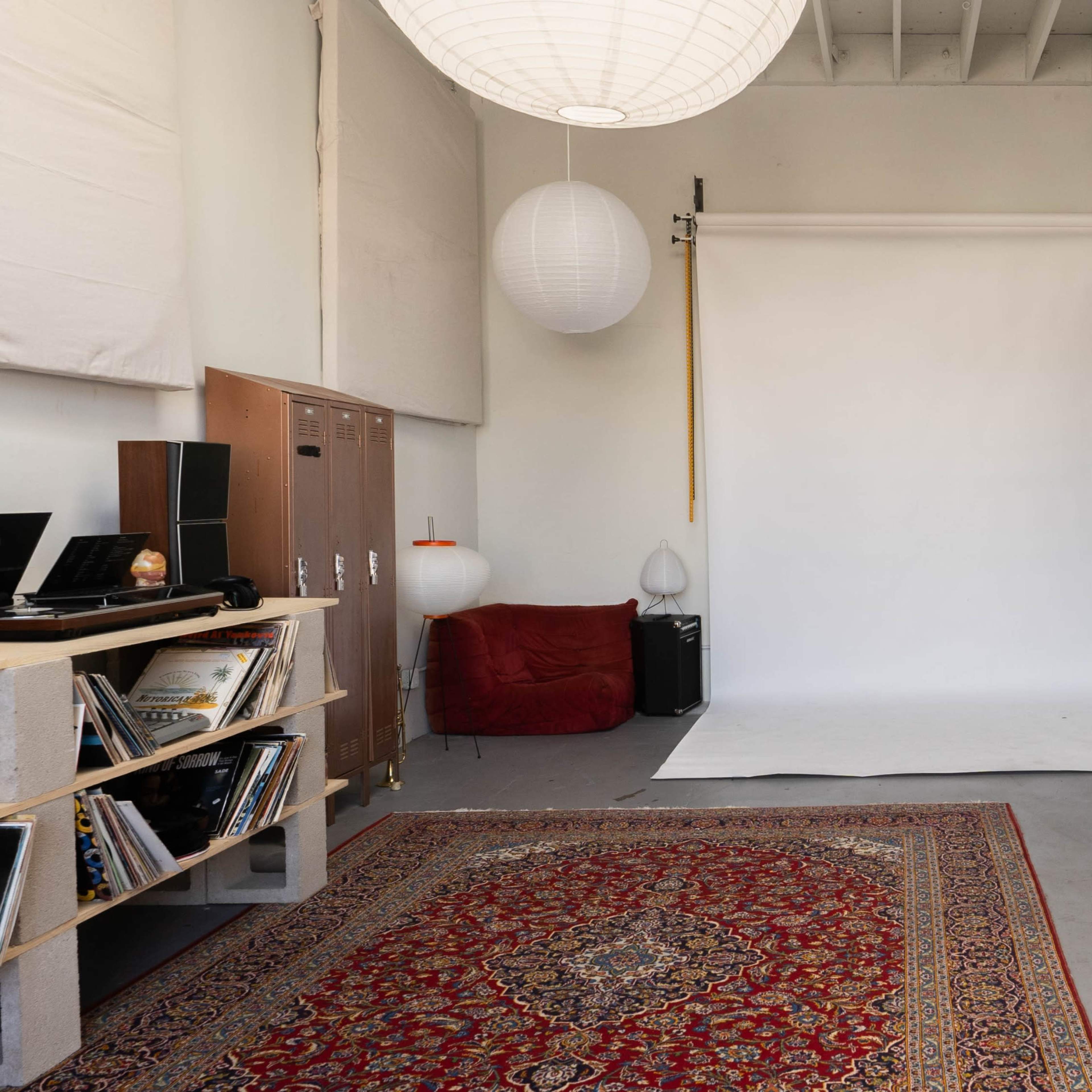 A spacious studio with a white backdrop, a wooden ladder, a patterned rug, and several hanging paper lanterns.