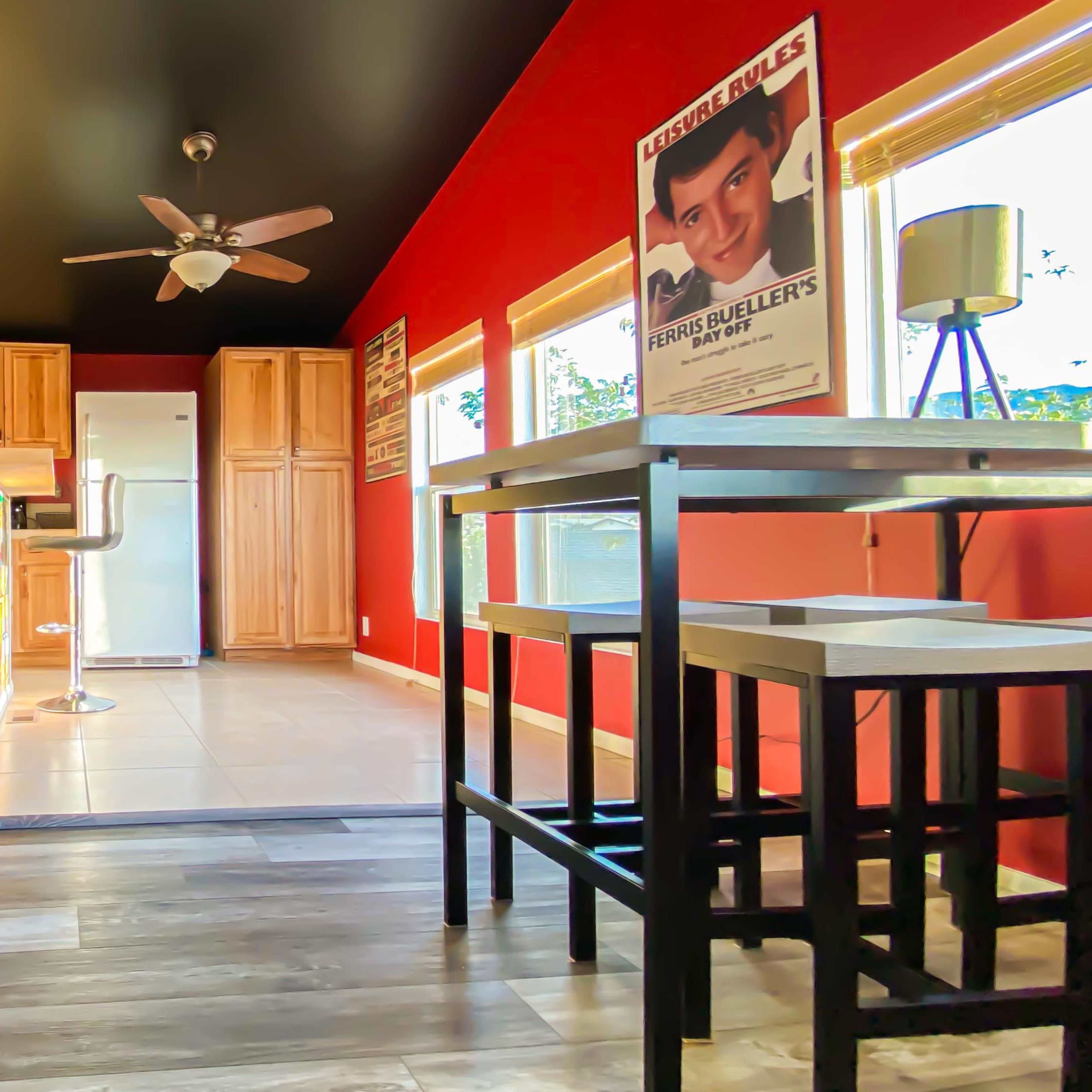 A kitchen with red walls, wooden cabinets, modern bar stools, and a table beside a window.