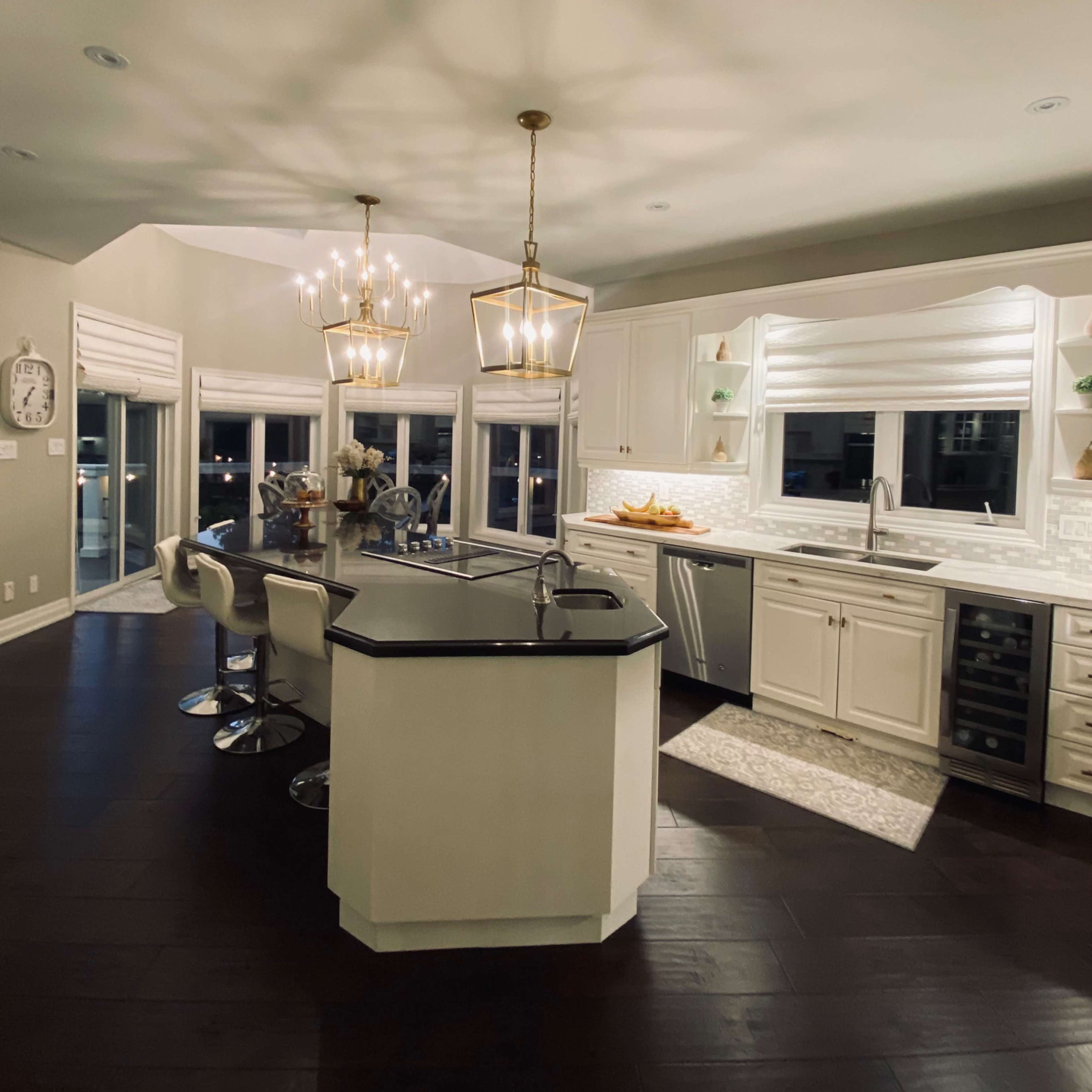 A modern kitchen features an island with bar stools, two pendant lights, and large windows providing natural light.