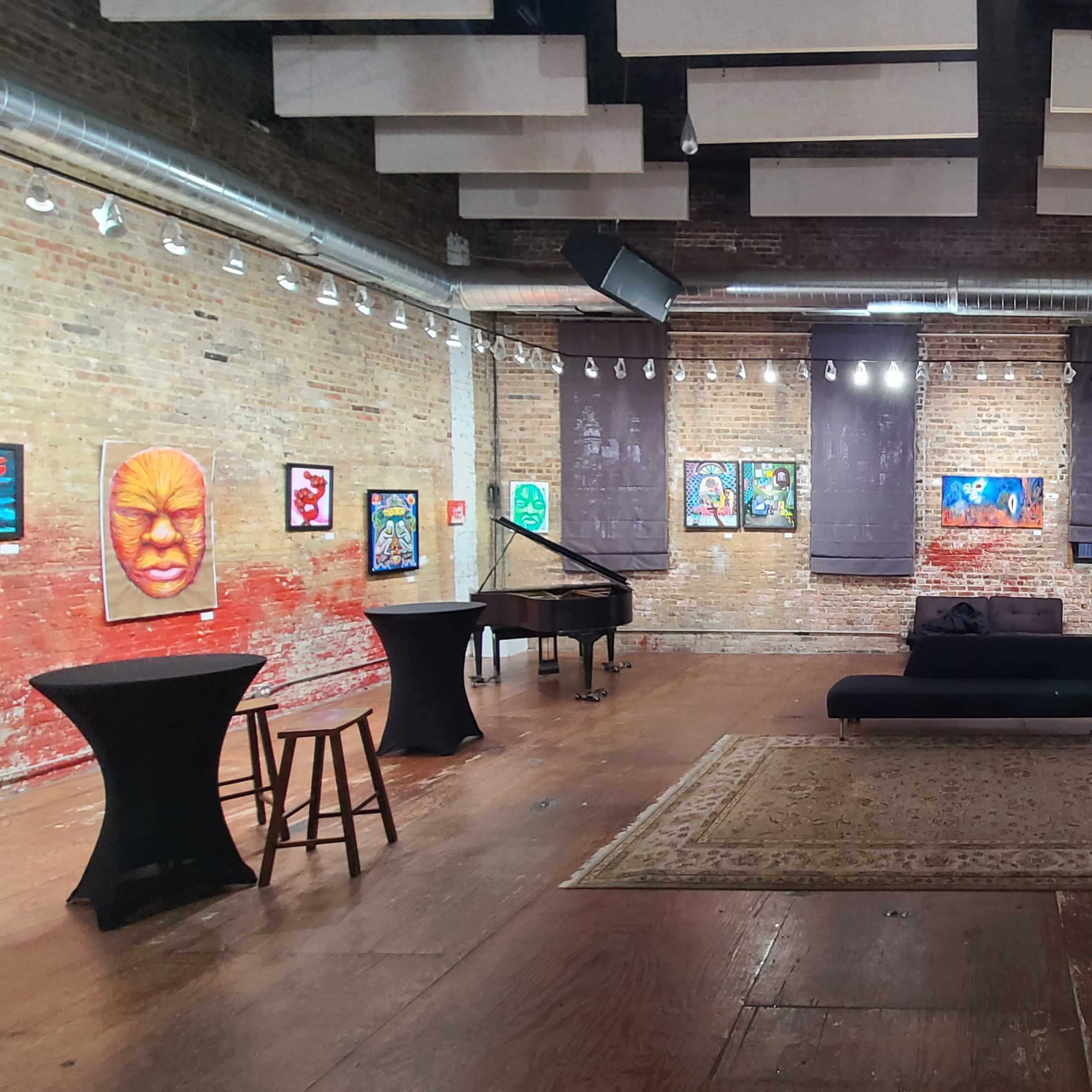 An art gallery featuring colorful paintings on the brick walls, with a piano and several lounge areas arranged around a central rug.
