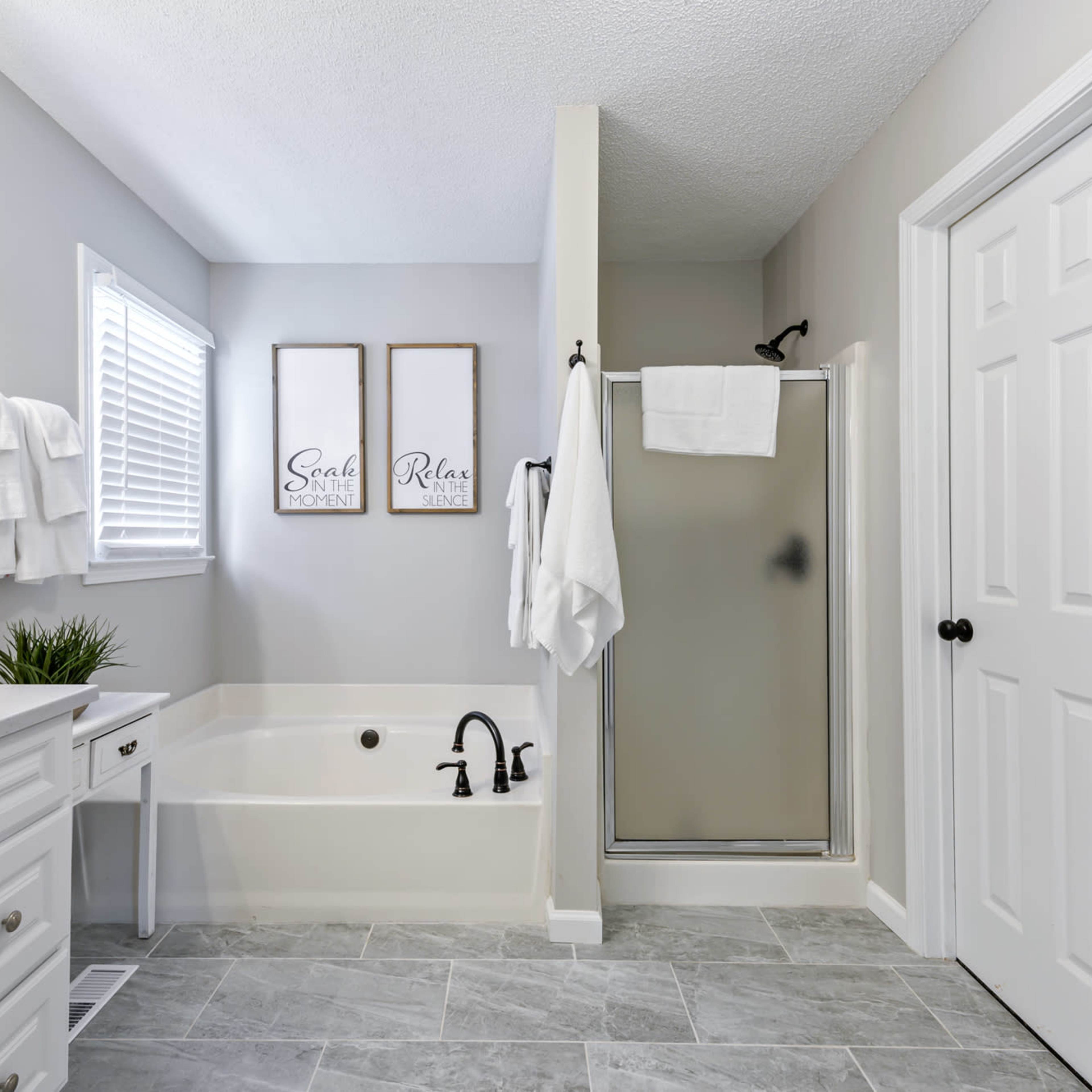 A modern bathroom featuring a bathtub, a glass shower enclosure, and a double vanity with decorative art on the wall.