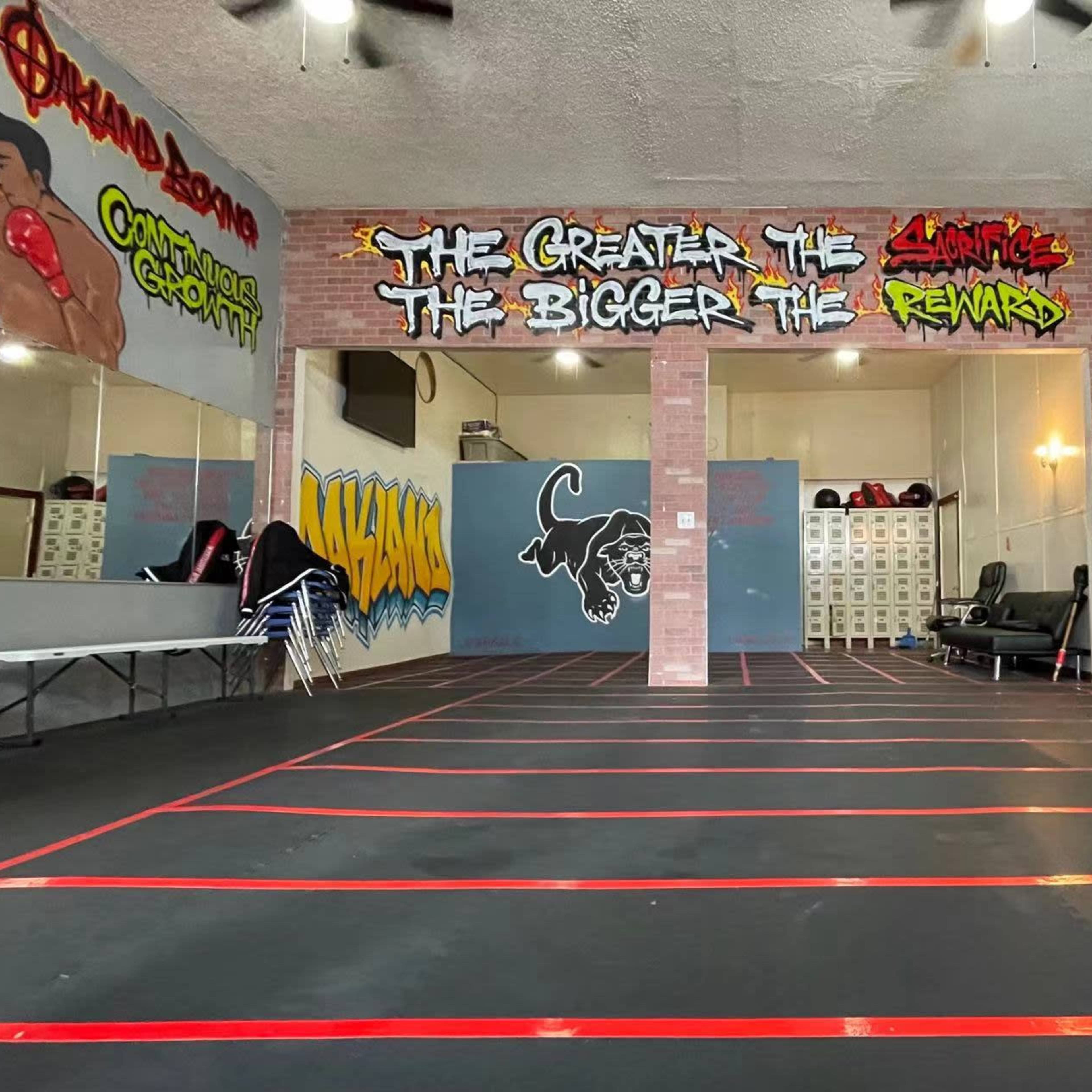 A gym interior with graffiti-covered walls and a spacious open area marked by red tape lines on the black floor.