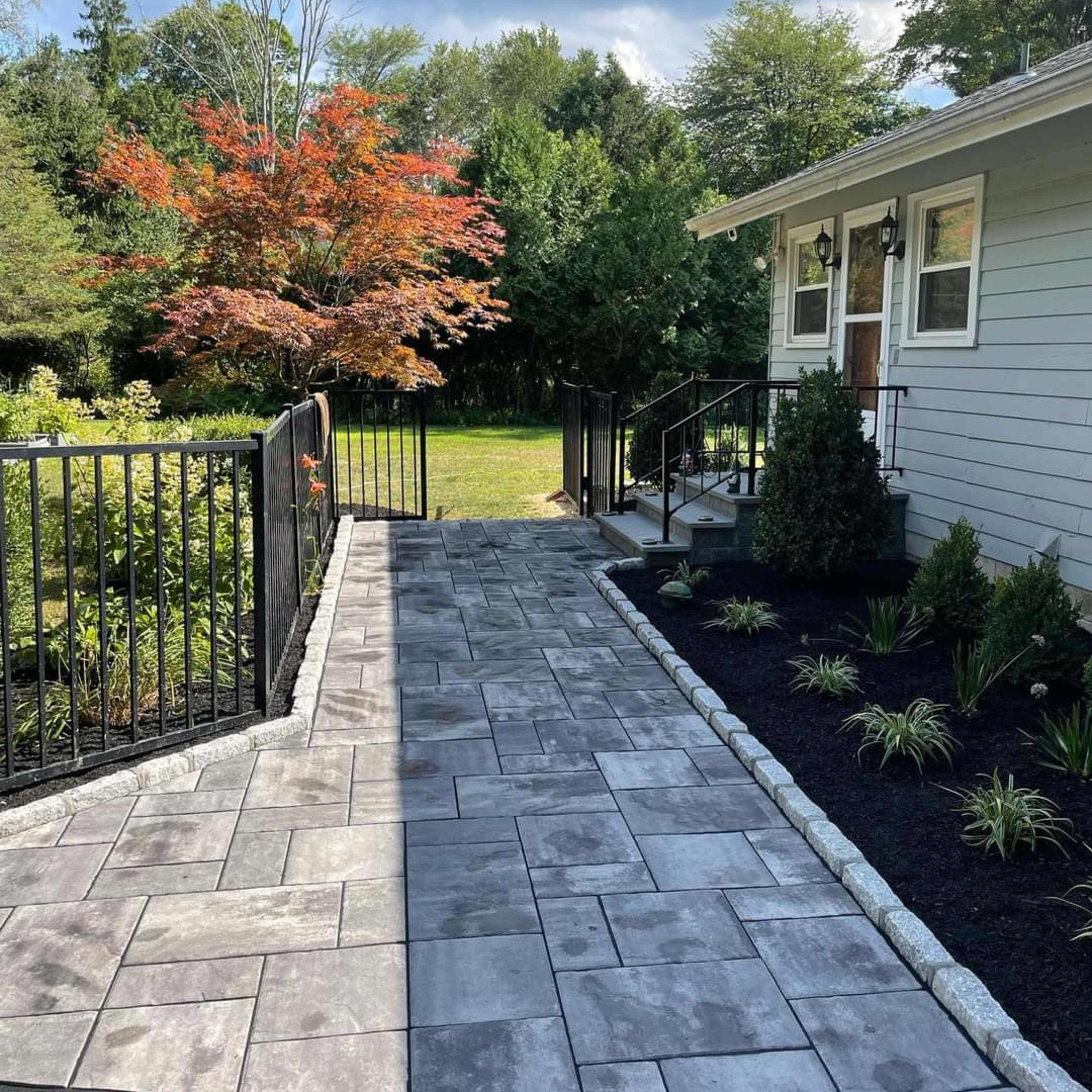 A stone pathway leads from a house to a landscaped garden with a railing and nearby shrubs.