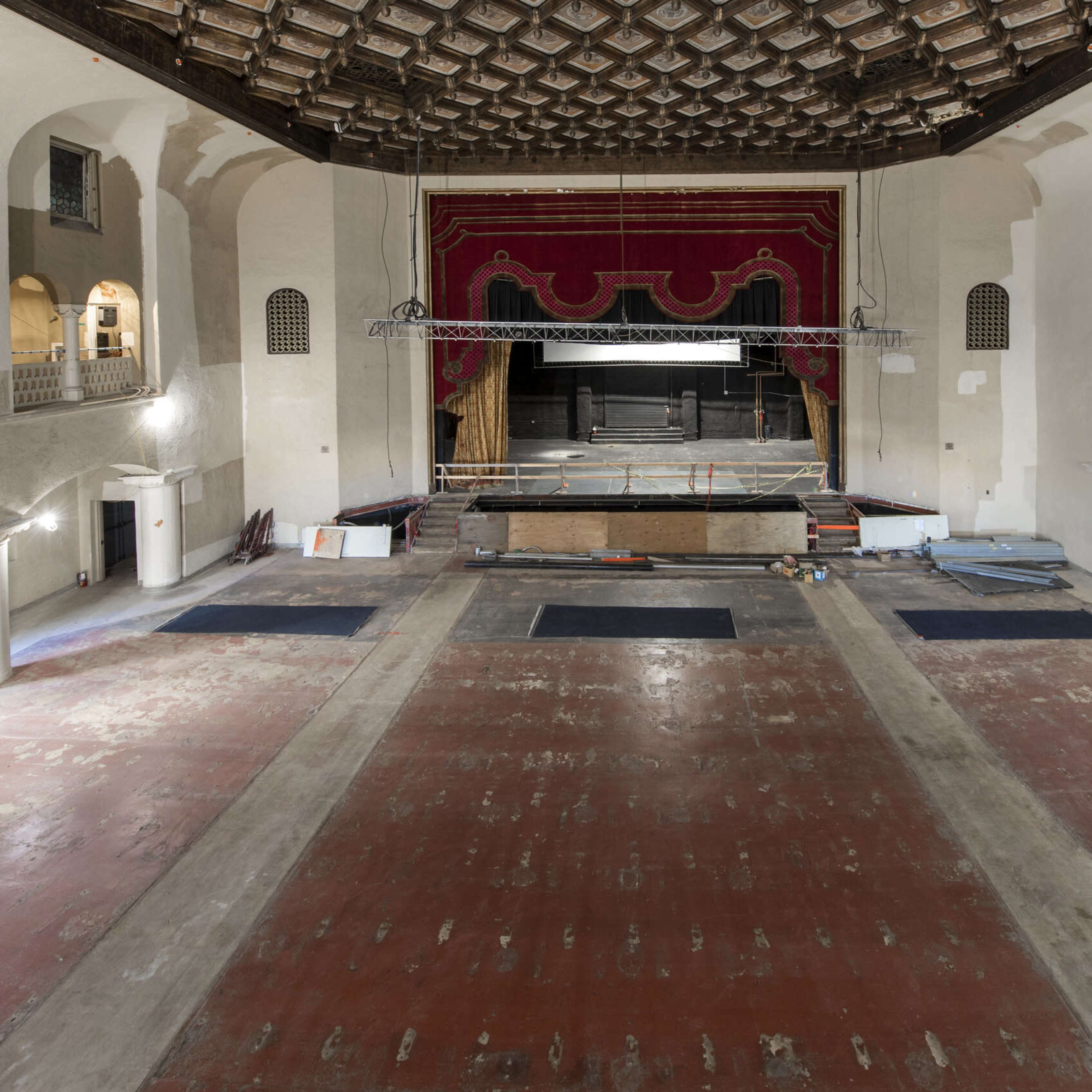 An empty theater with a stage at the front, adorned with red curtains, and a spacious, bare wooden floor.