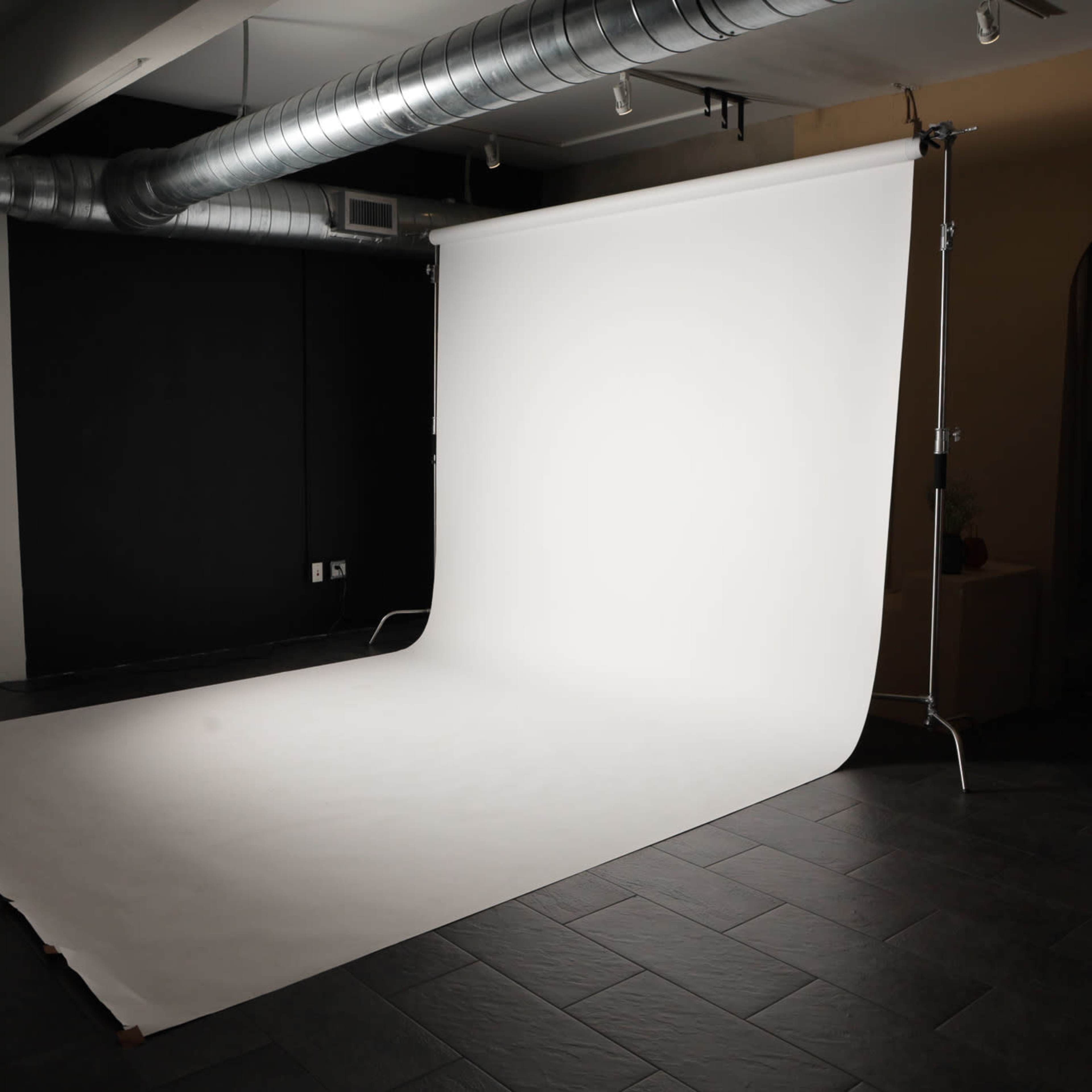 A photography studio with a white backdrop, softbox lighting, and a dark wall.