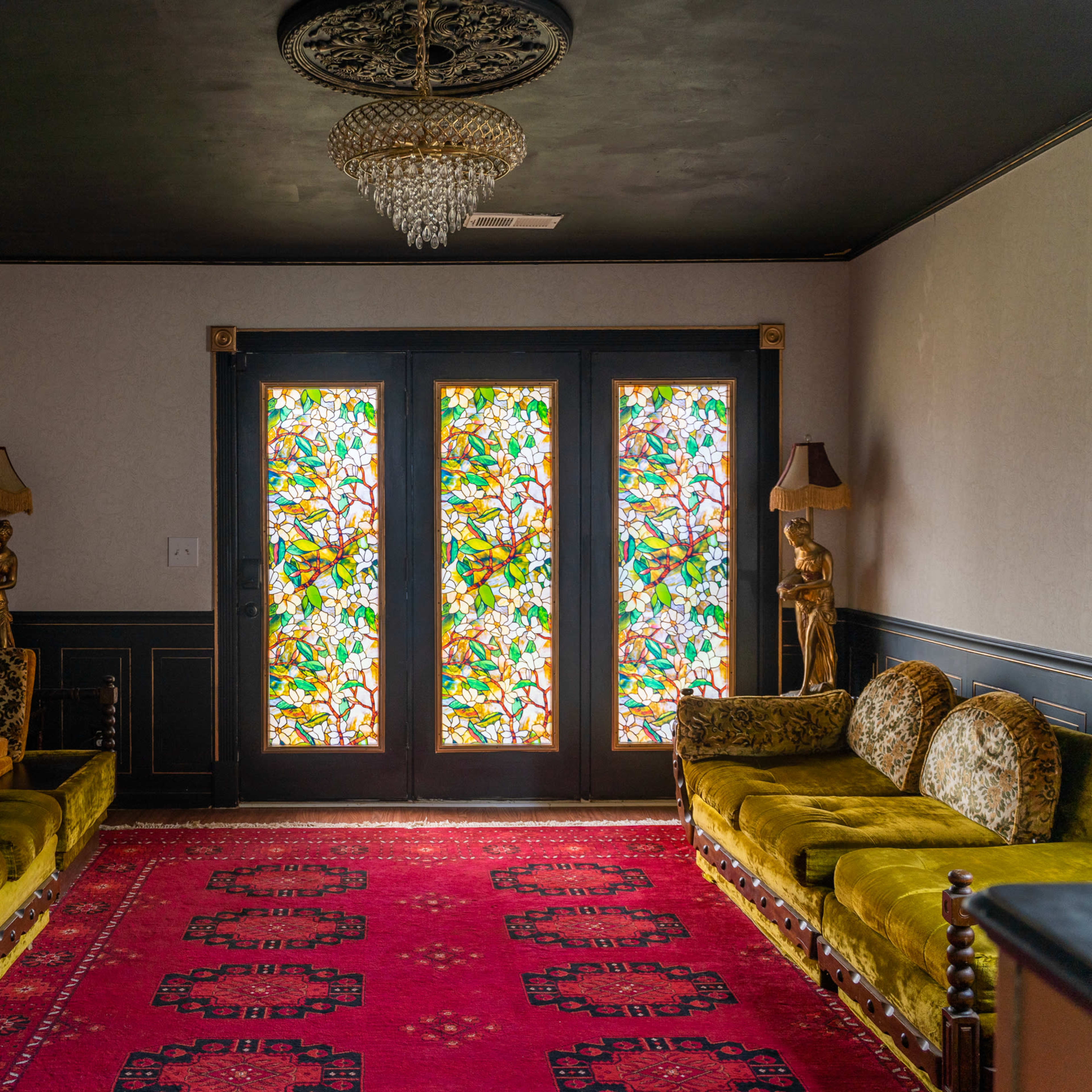 The room features a red carpet, green velvet sofas, and ornate stained glass doors adorned with intricate designs.