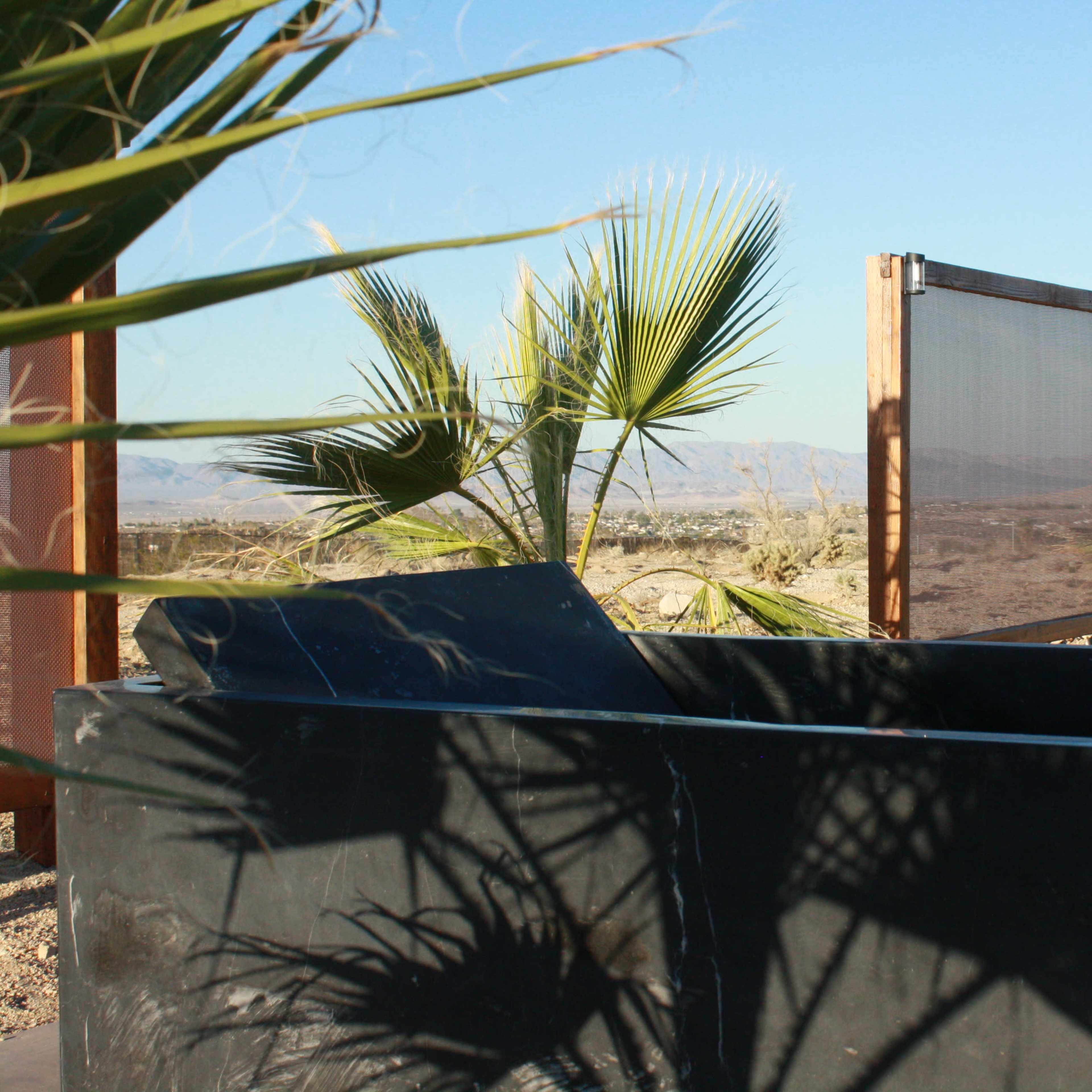 A modern black stone structure with palm trees and wooden screens set against a desert landscape.