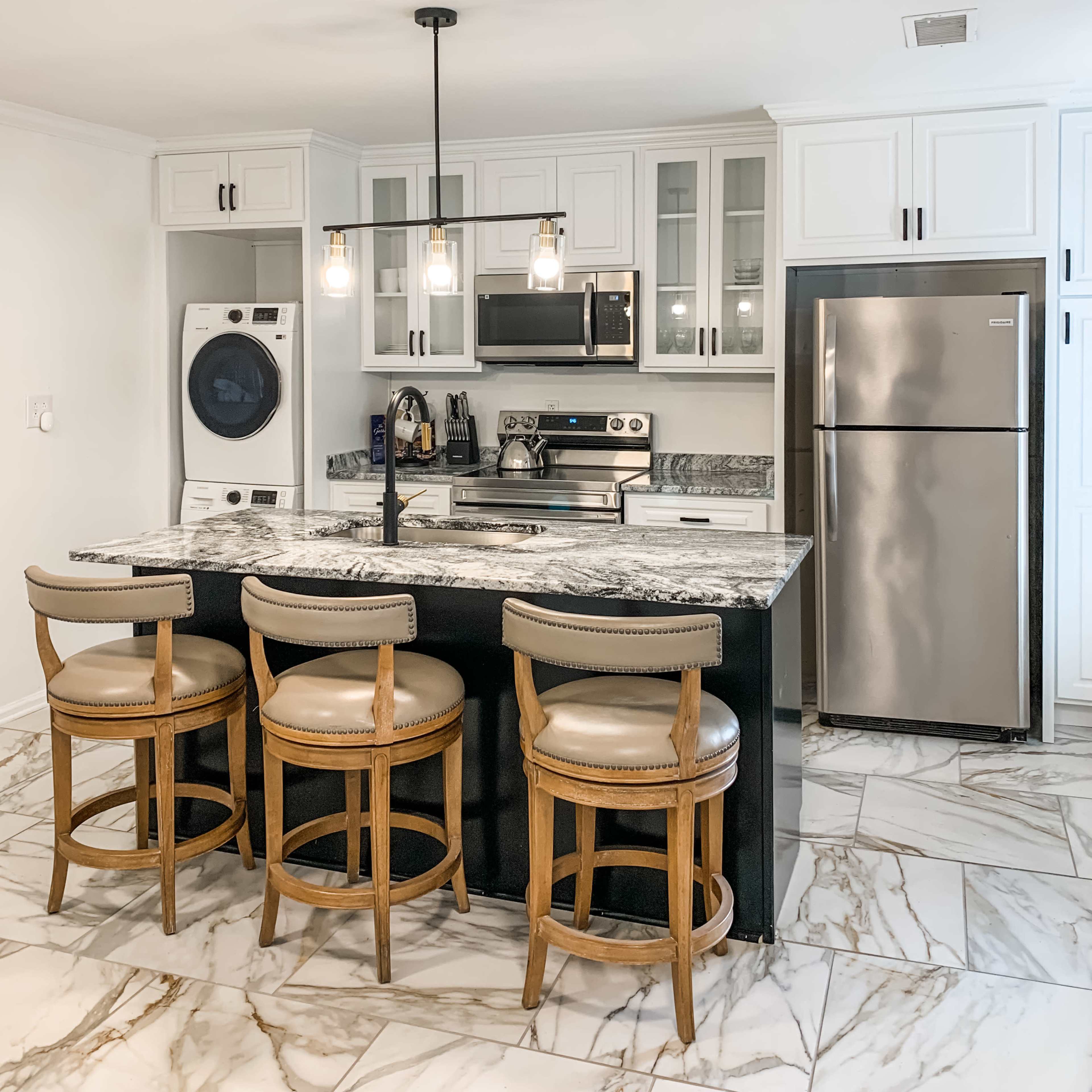 The kitchen features stainless steel appliances, a marble countertop island with seating, and a combination washer and dryer unit.