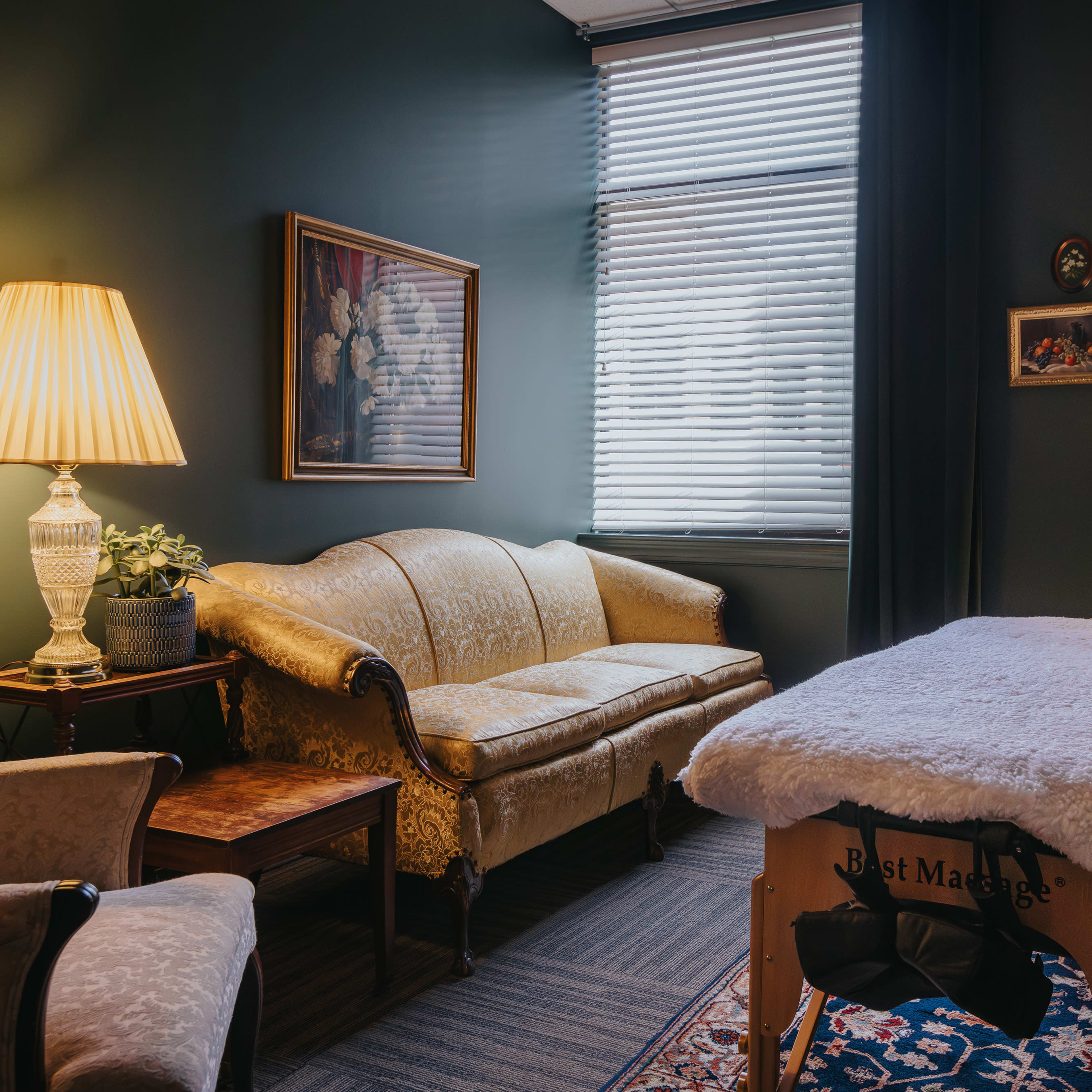 A cozy massage therapy room with a sofa, an armchair, and a massage table draped with a soft covering.