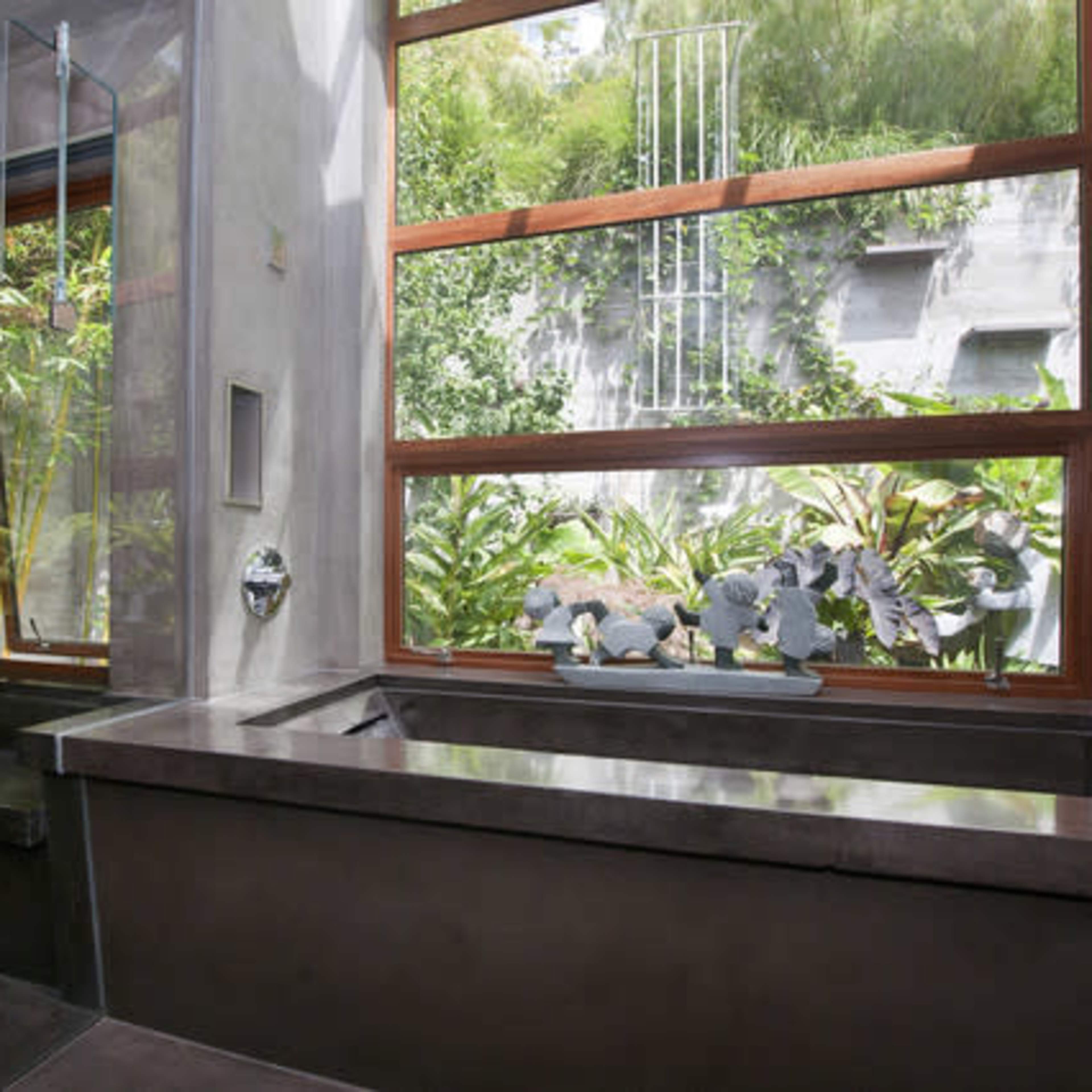 A modern bathroom featuring a large bathtub, large windows with a view of greenery, and a minimalist design.