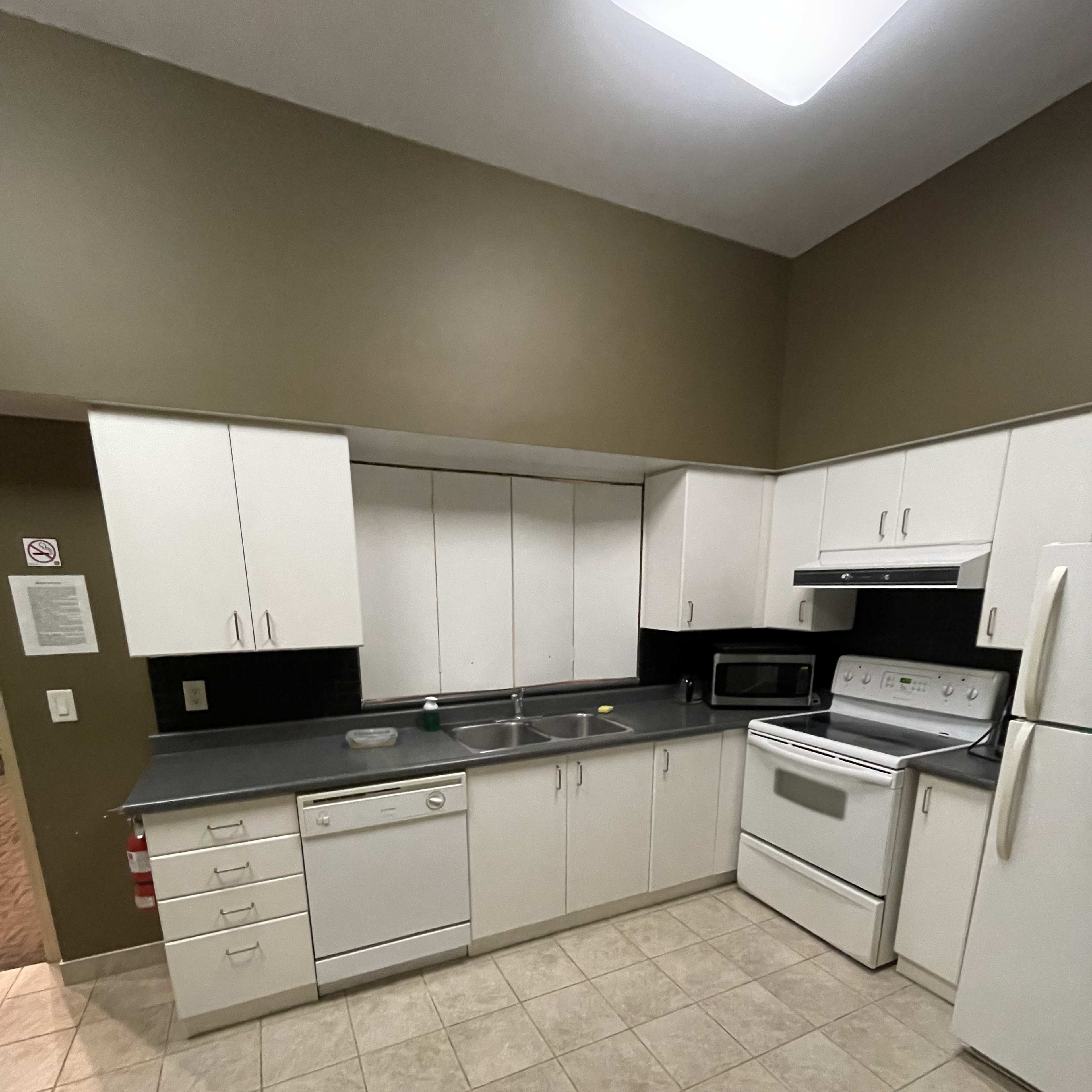 A kitchen with white cabinetry, a black countertop, and standard appliances including a dishwasher, stove, microwave, and refrigerator.