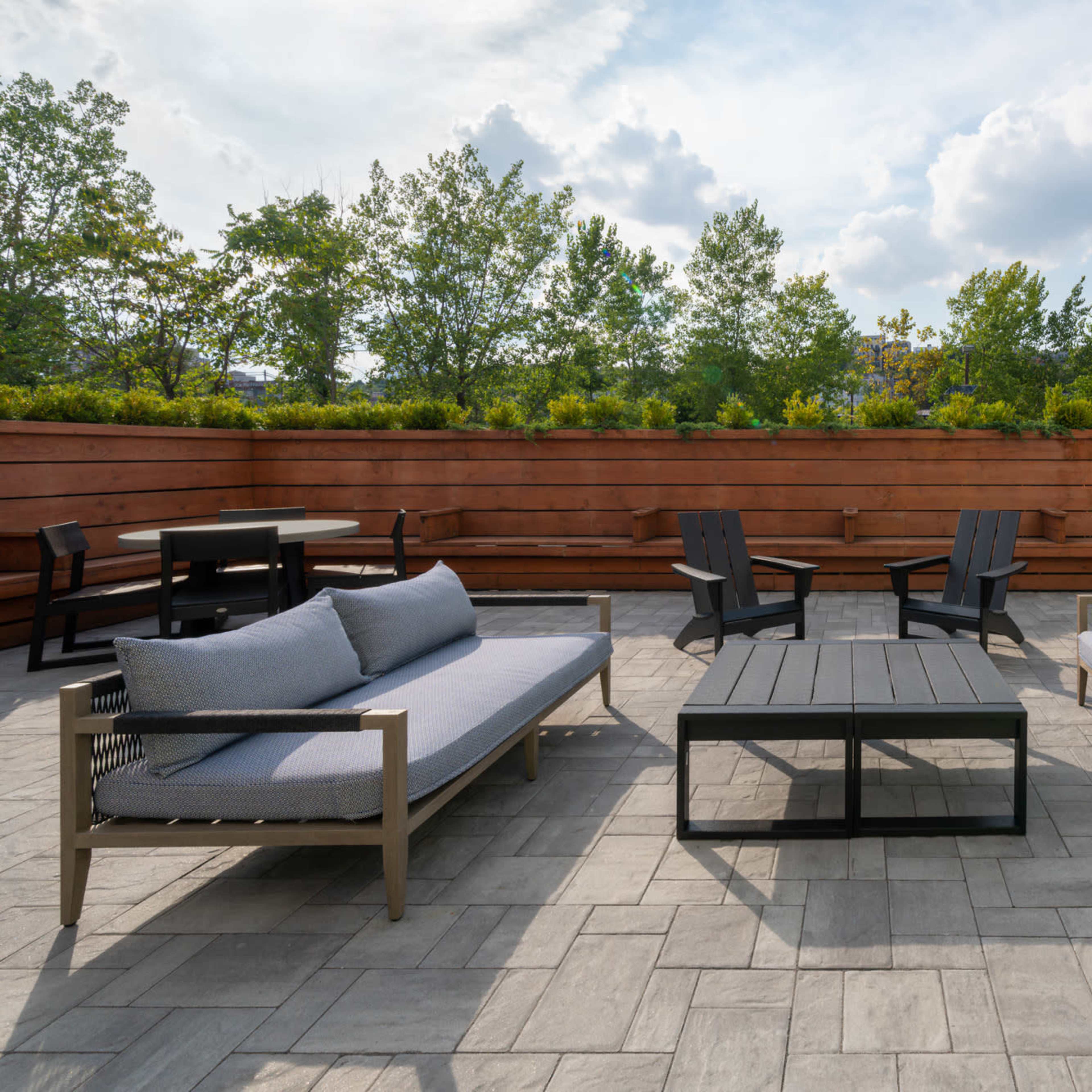 A spacious outdoor lounge area with gray sofas and a coffee table surrounded by trees and a wooden fence.