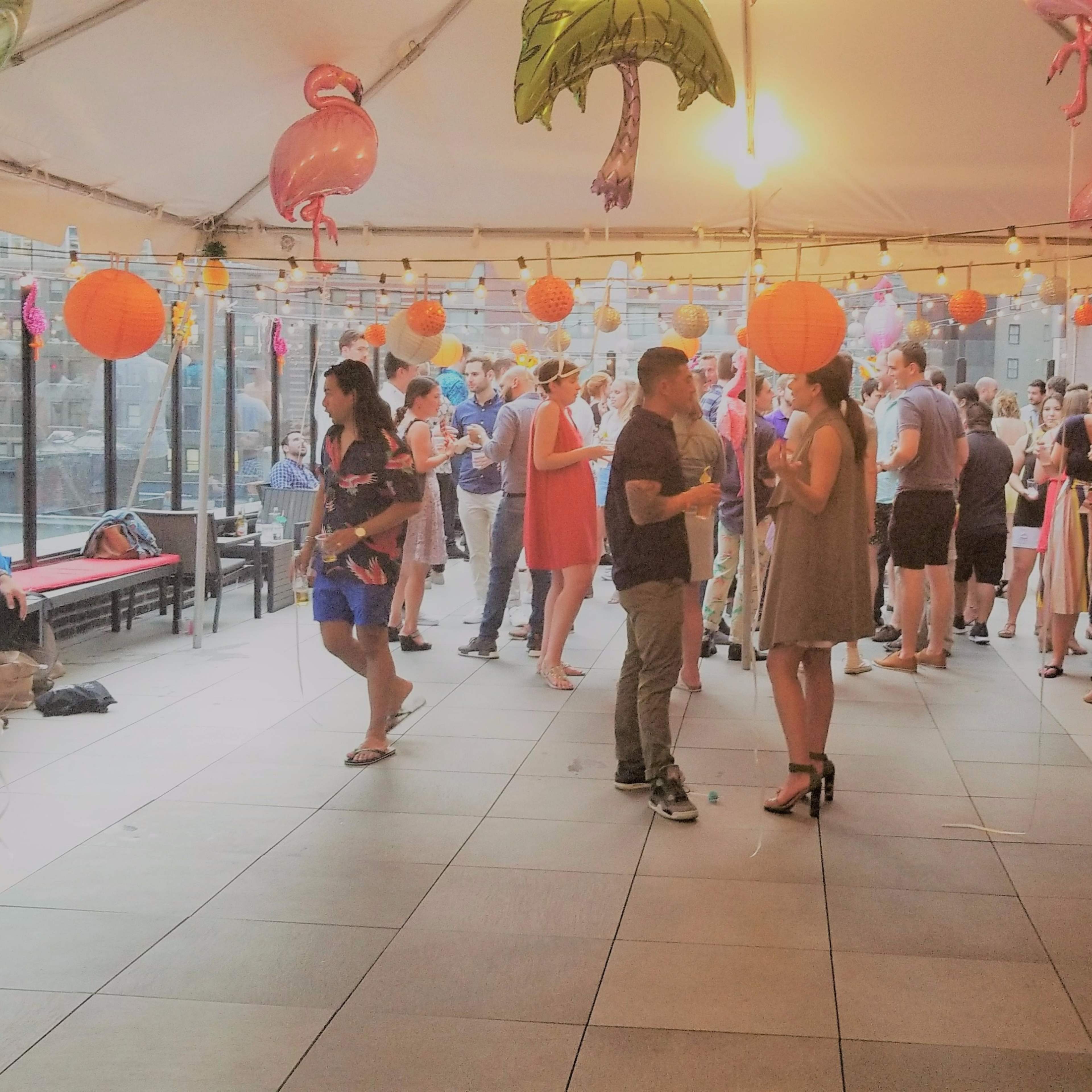A tented rooftop party features guests mingling under colorful decorations and hanging lanterns.