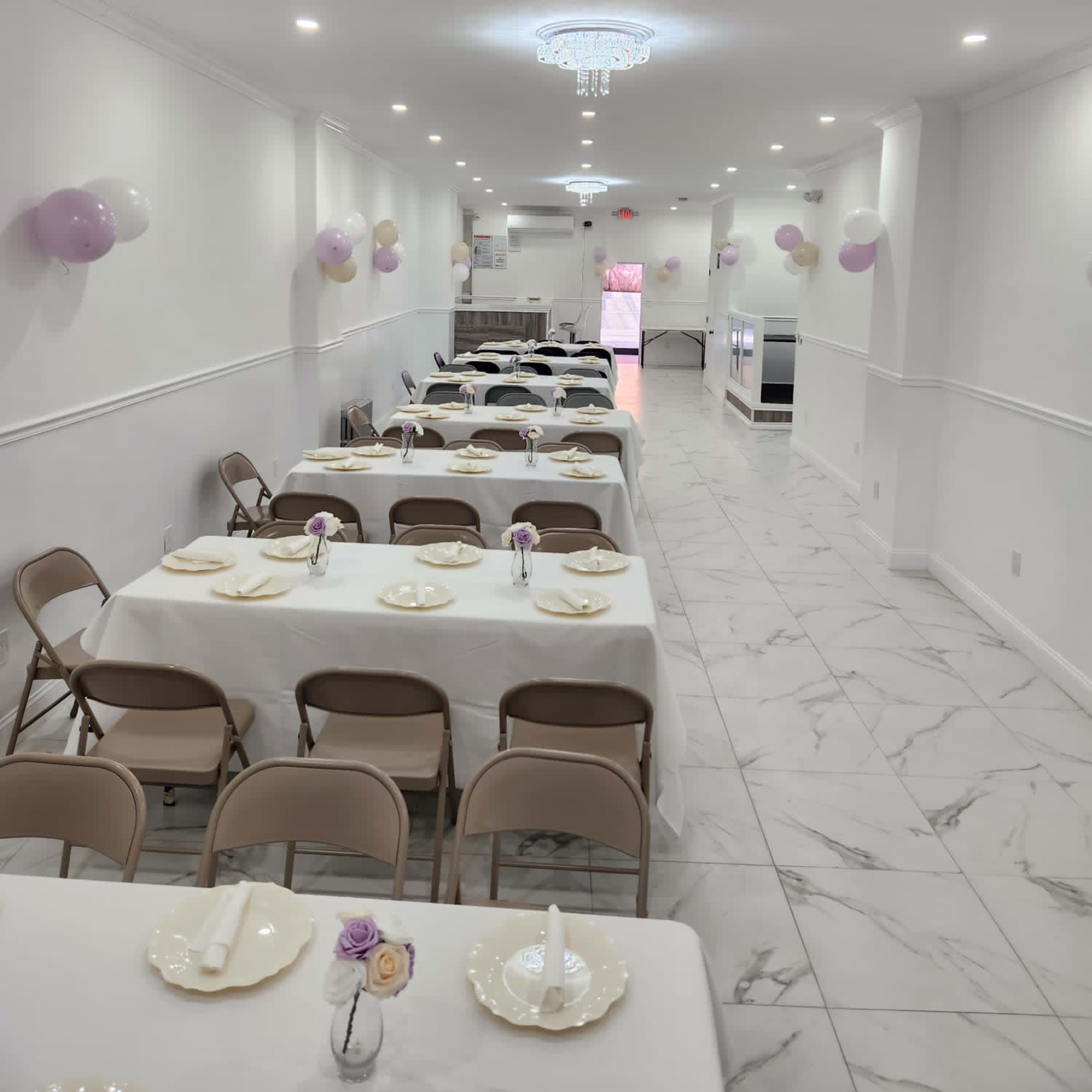 A long, narrow banquet hall with neatly arranged tables covered in white tablecloths and decorated with small floral centerpieces.