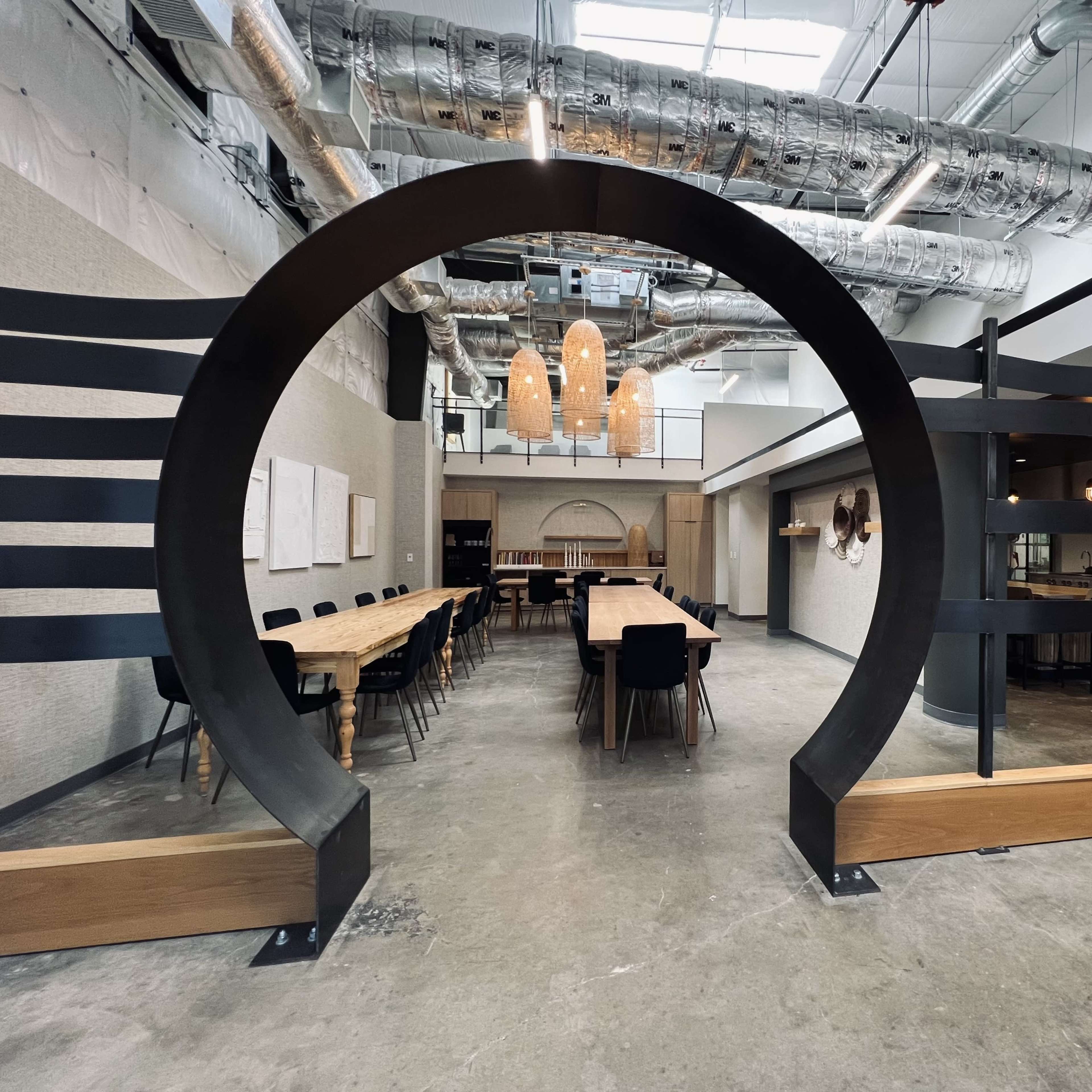 A modern interior of a restaurant featuring a large circular arch, a long communal table, and various seating arrangements.