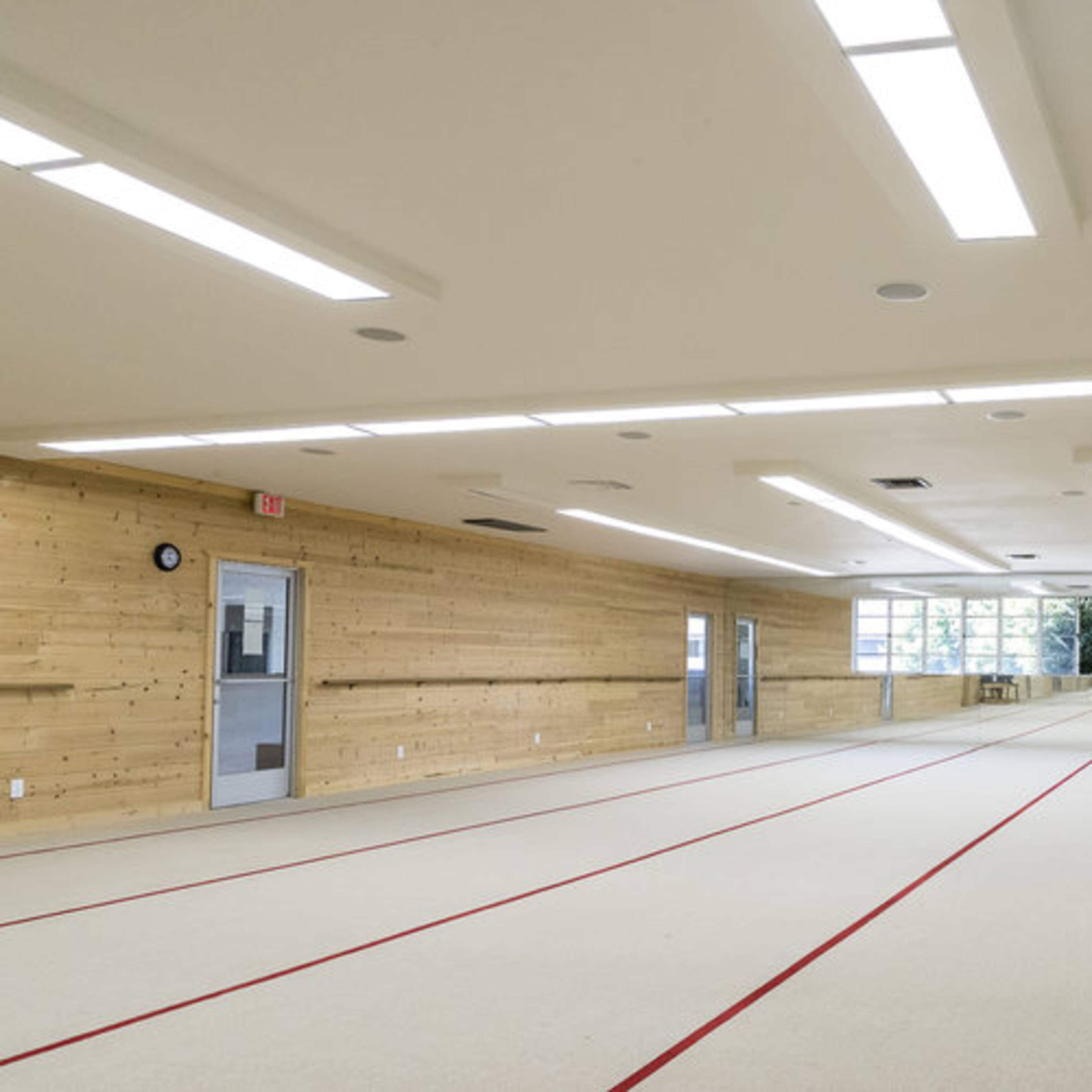 A spacious indoor gymnasium with wooden walls, a mirrored wall, and red lines marking a practice area on the floor.