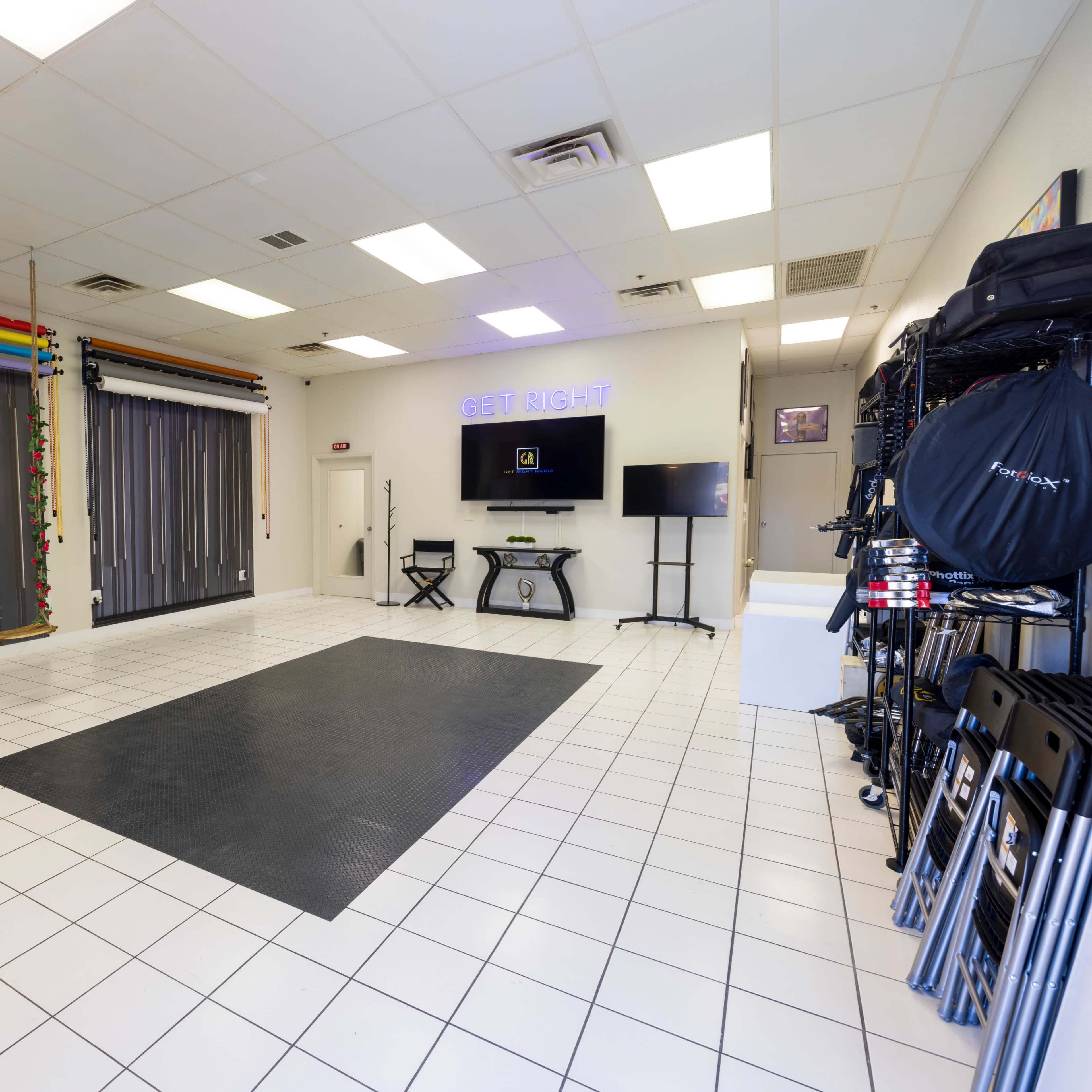 A spacious, well-lit studio with a black mat on the floor, colorful backdrop strips on the wall, and various equipment neatly arranged on the side.