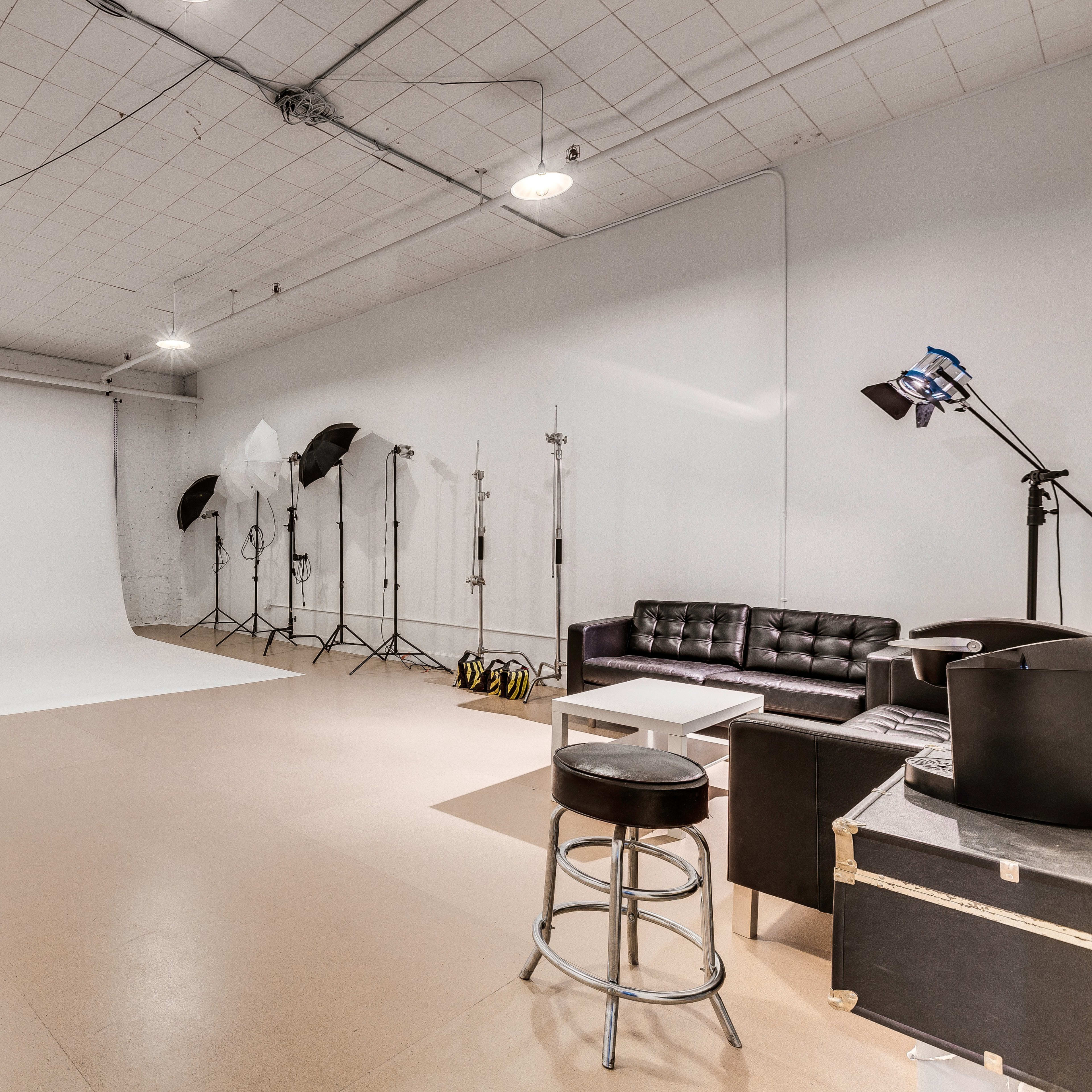 A spacious photography studio with a white backdrop, lighting equipment, and a black couch.